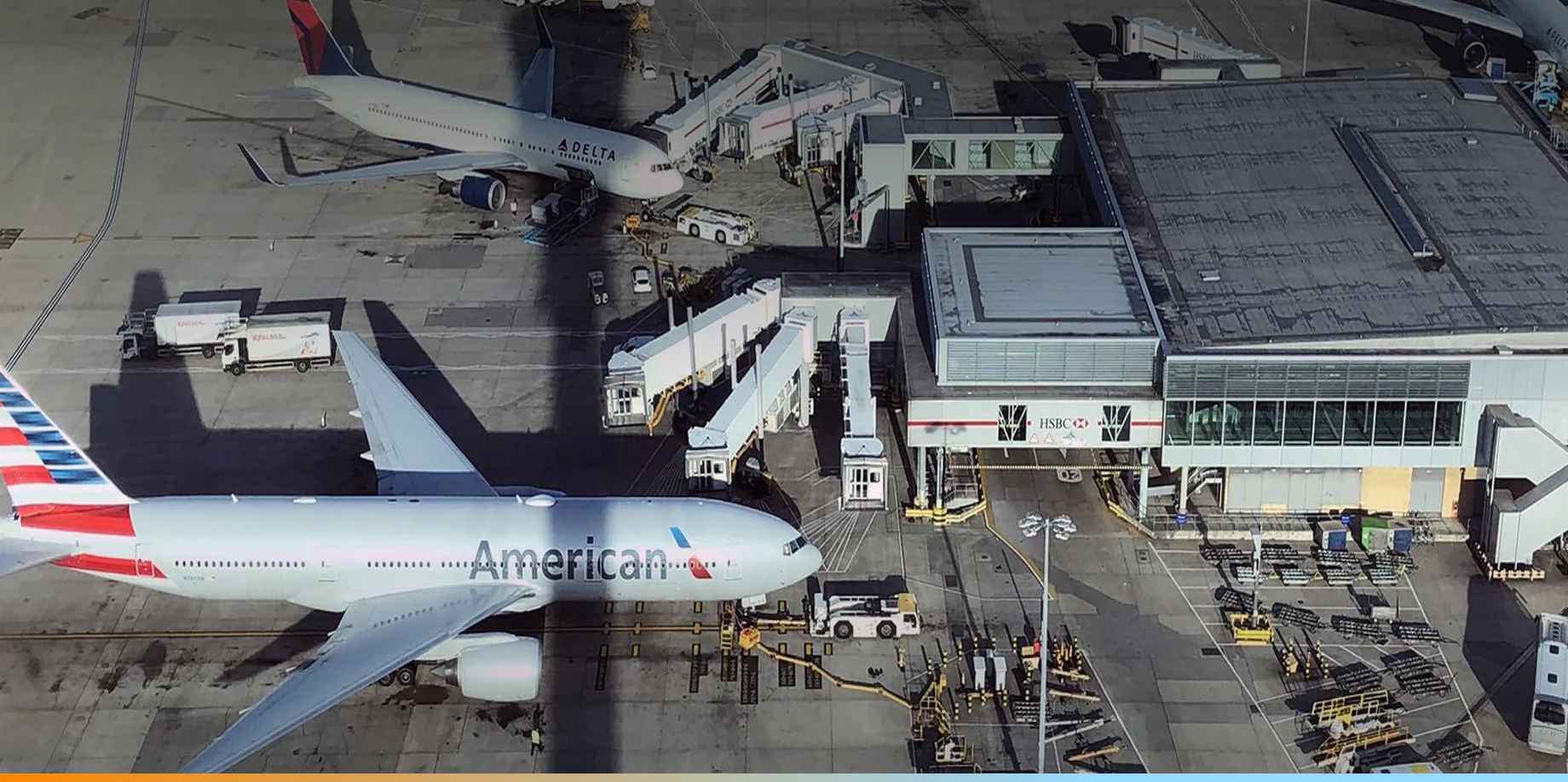 Aerial view of American Airlines and Delta Airlines planes parked at airport gates surrounded by service vehicles and equipment.