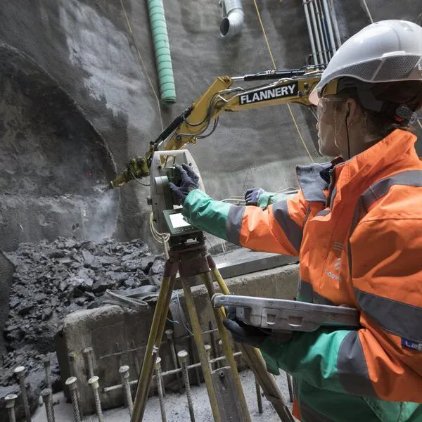 Person in orange safety jacket operating surveying equipment inside an underground construction site.