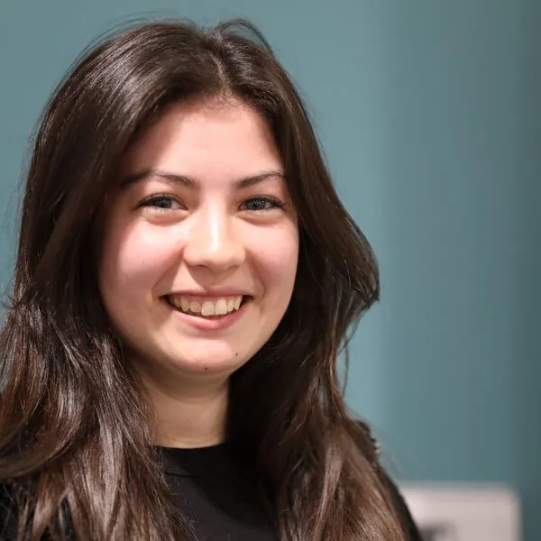 Close-up portrait of a smiling person against a teal background.