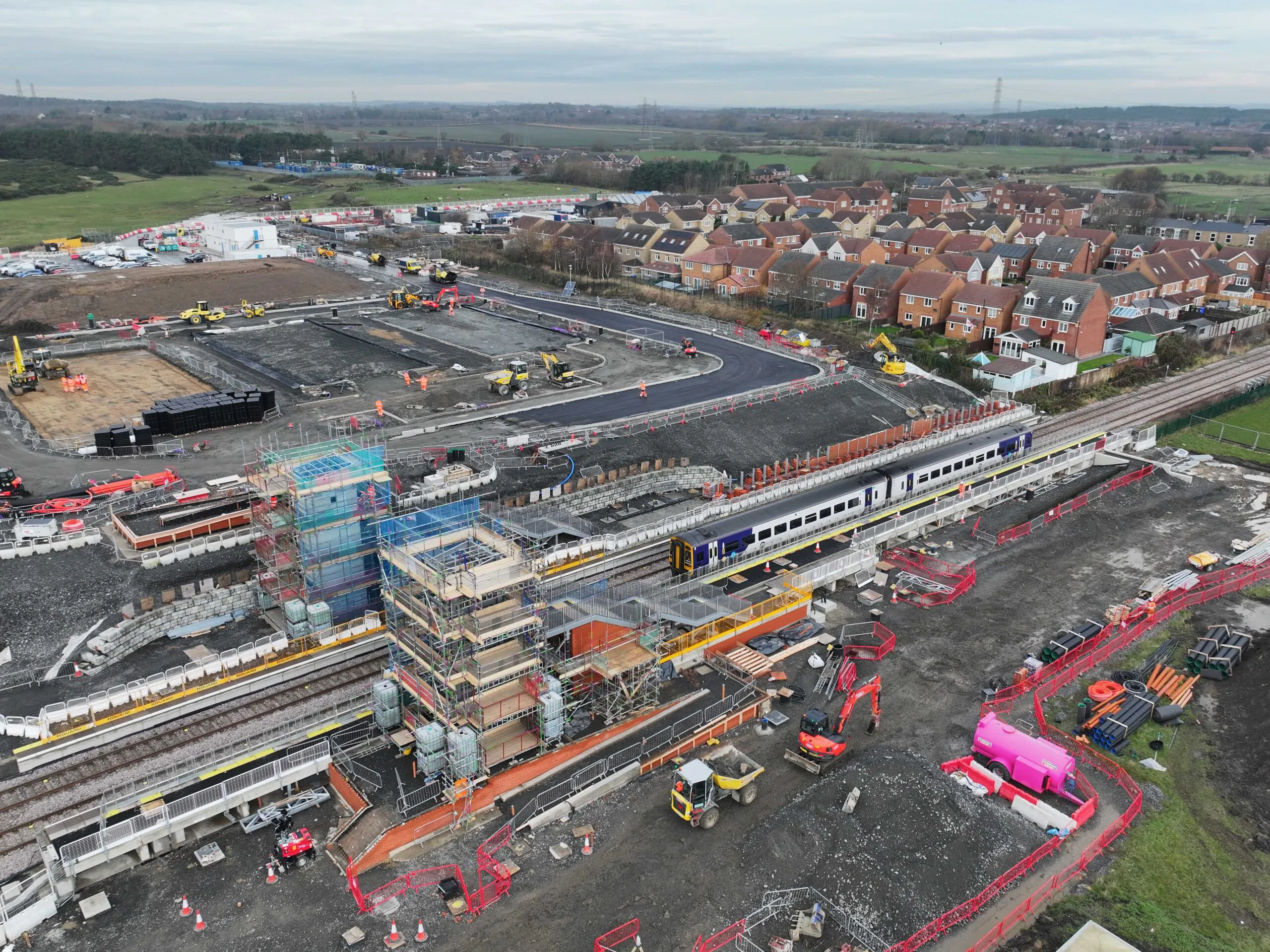 Aerial view of railway-side construction near residential areas with scaffolding and heavy machinery.
