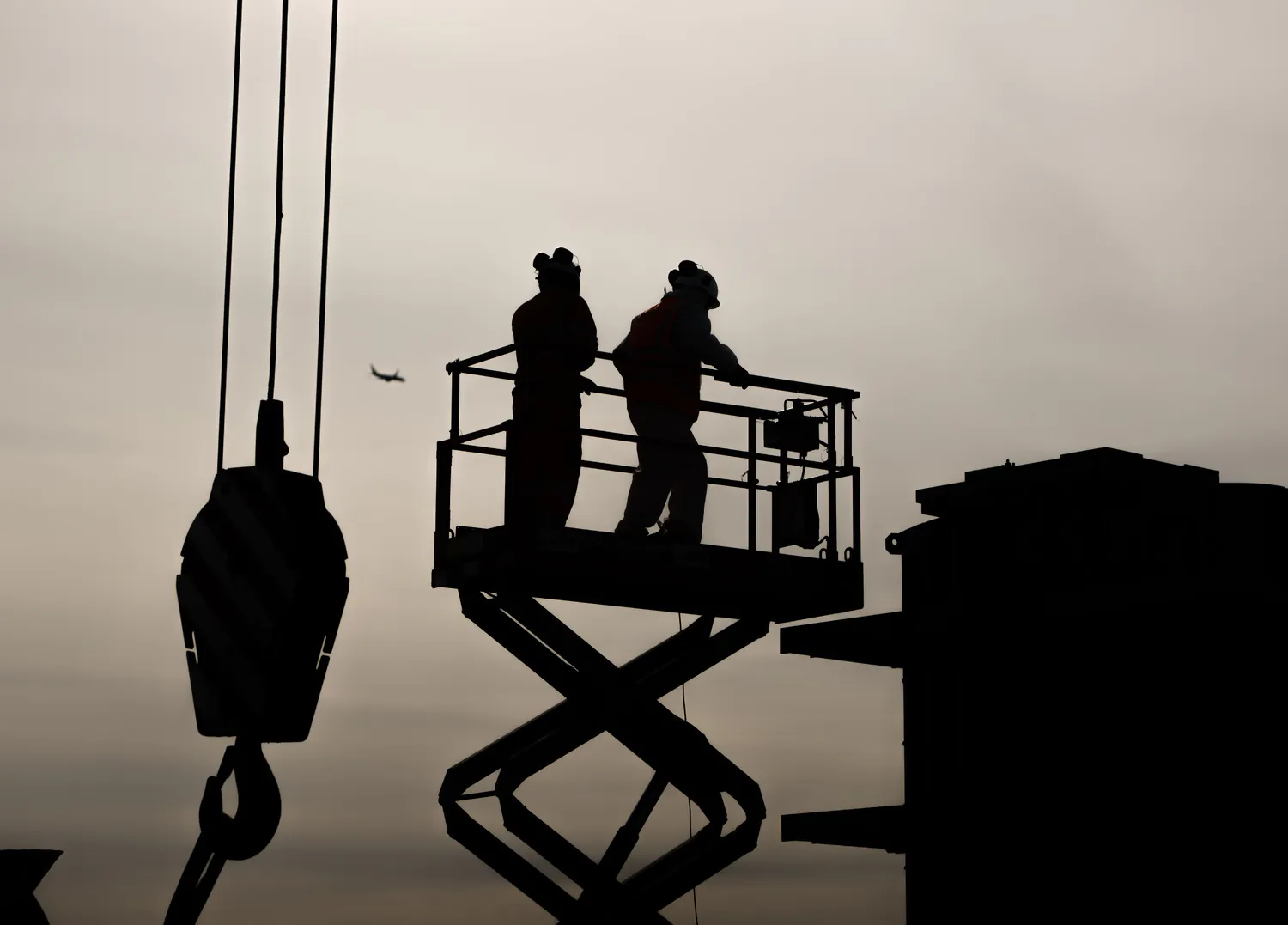 Worker inspecting a steel beam installation at a construction site with scaffolding in the background.