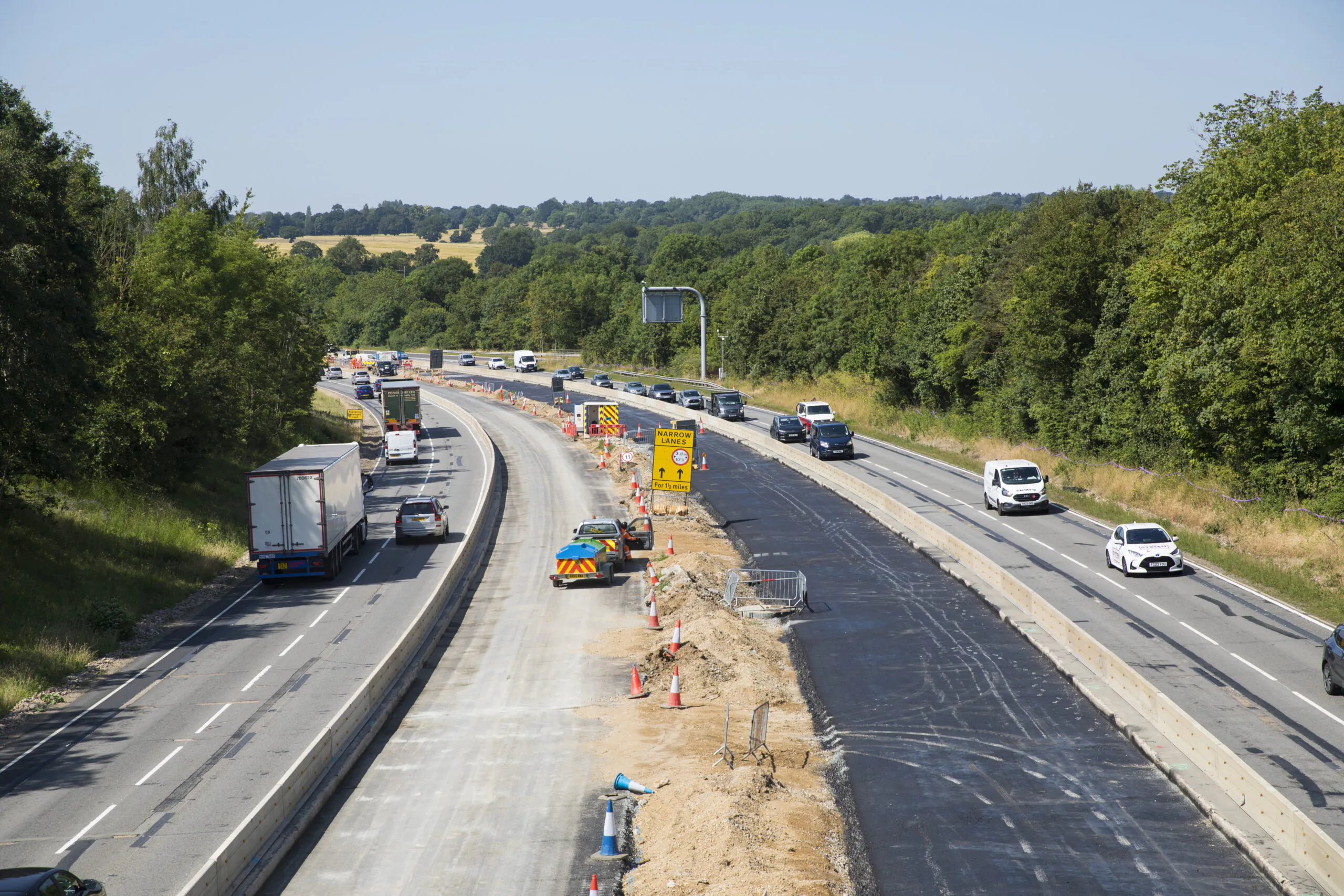 Highway under construction with vehicles on one side and construction equipment on the other side.