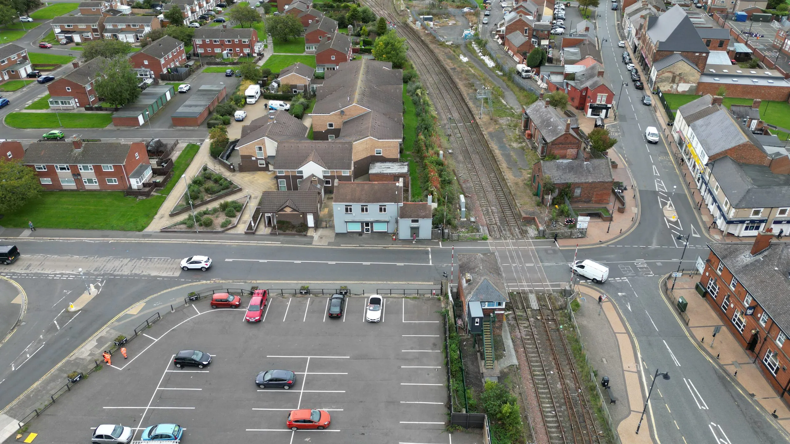Aerial view of a residential area with houses, a parking lot, and a railway line running through the middle with a visible crossing.