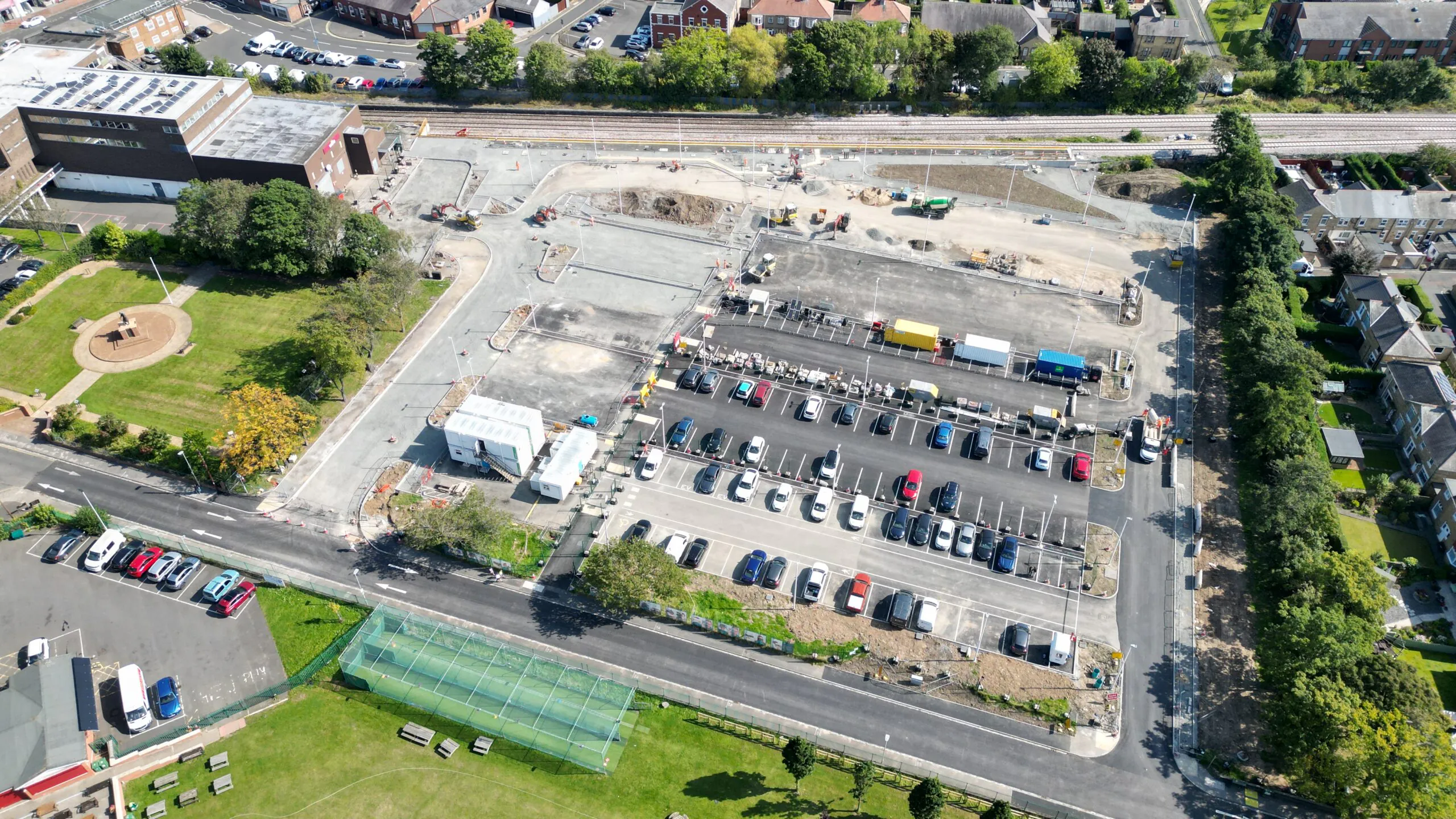 Aerial view of railway-side construction with heavy machinery and workers operating near residential buildings.
