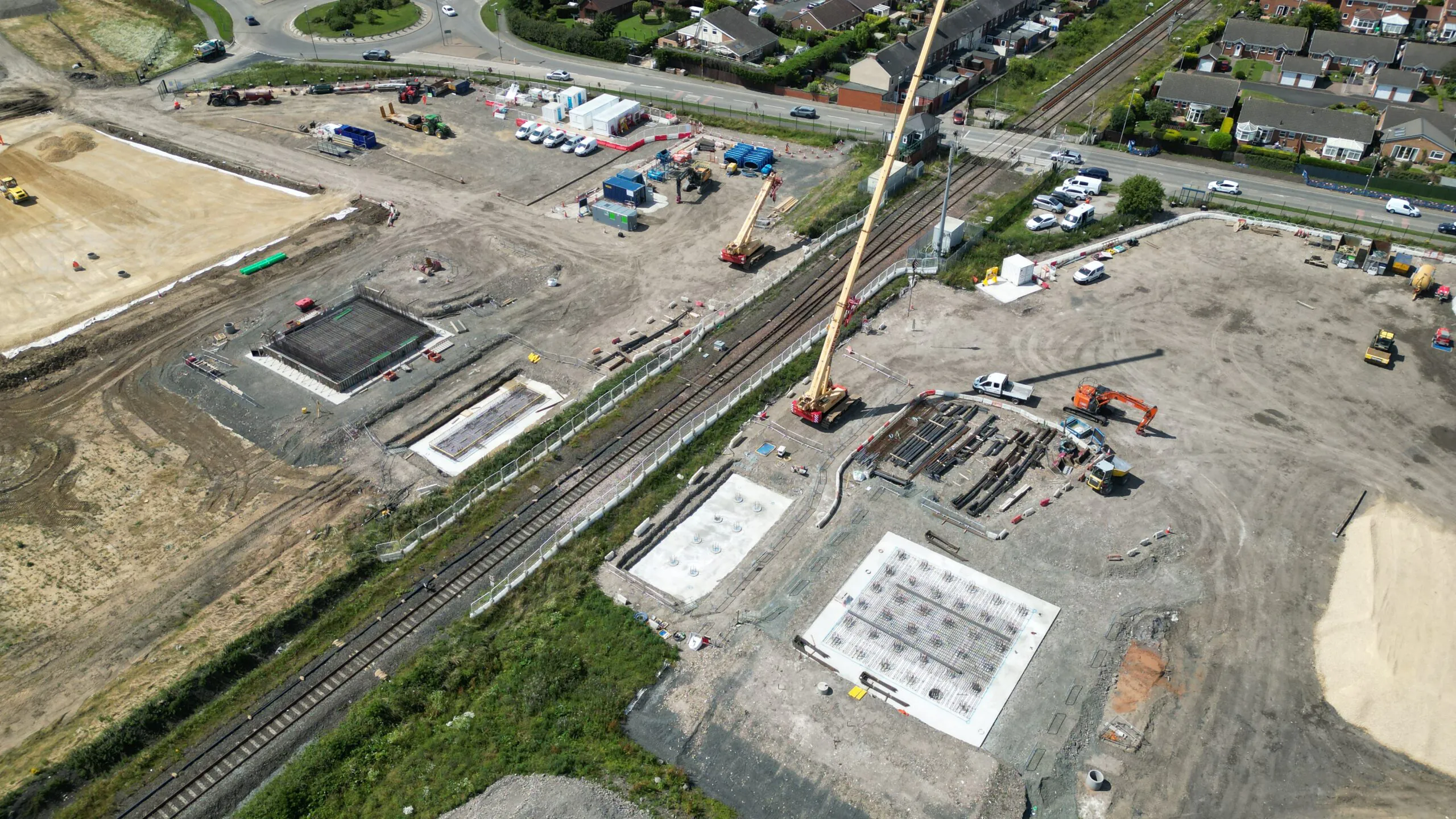 Aerial view of railway tracks running through a large construction site with foundations and heavy machinery.