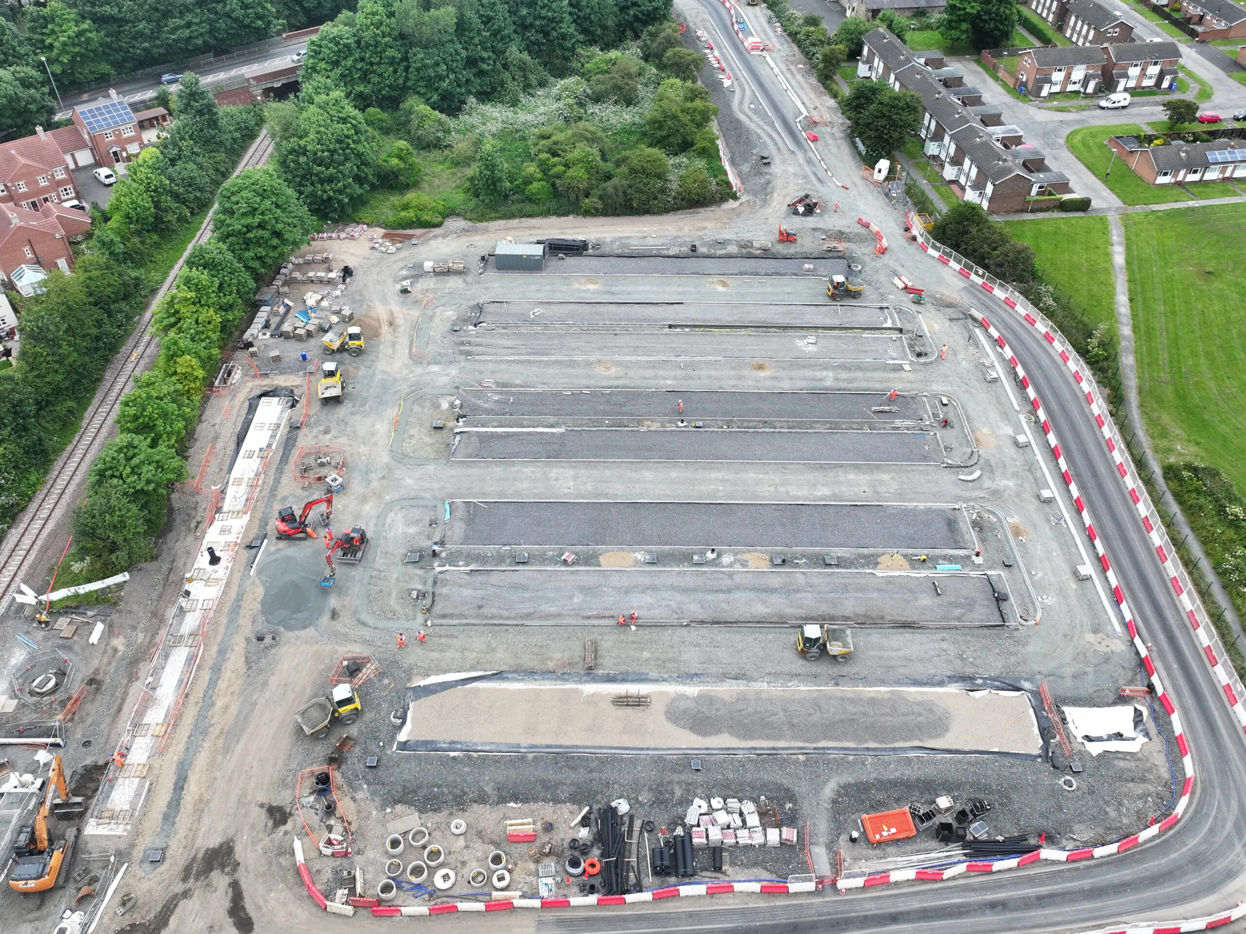 Aerial view of a large construction site with multiple active zones, surrounded by trees and residential areas.