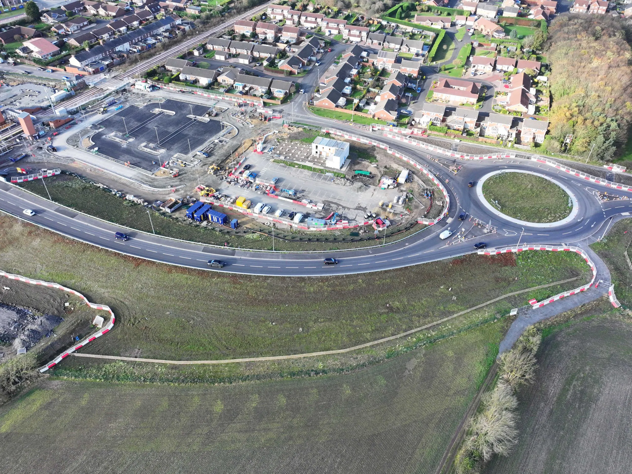 Aerial view of construction site with multiple access roads, temporary buildings, and surrounding fields.