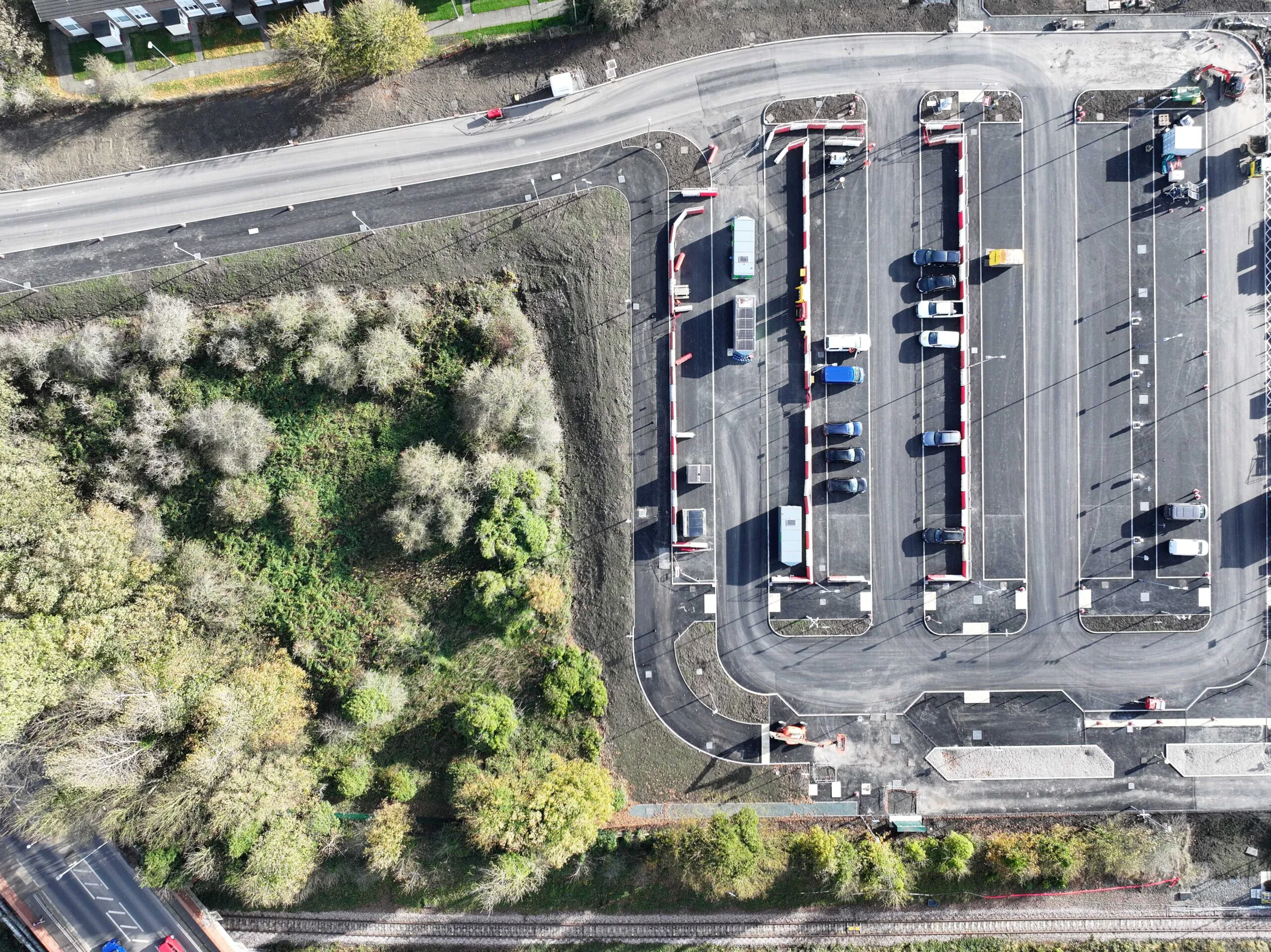 Overhead view of a partially completed car park with marked lanes next to a wooded area.