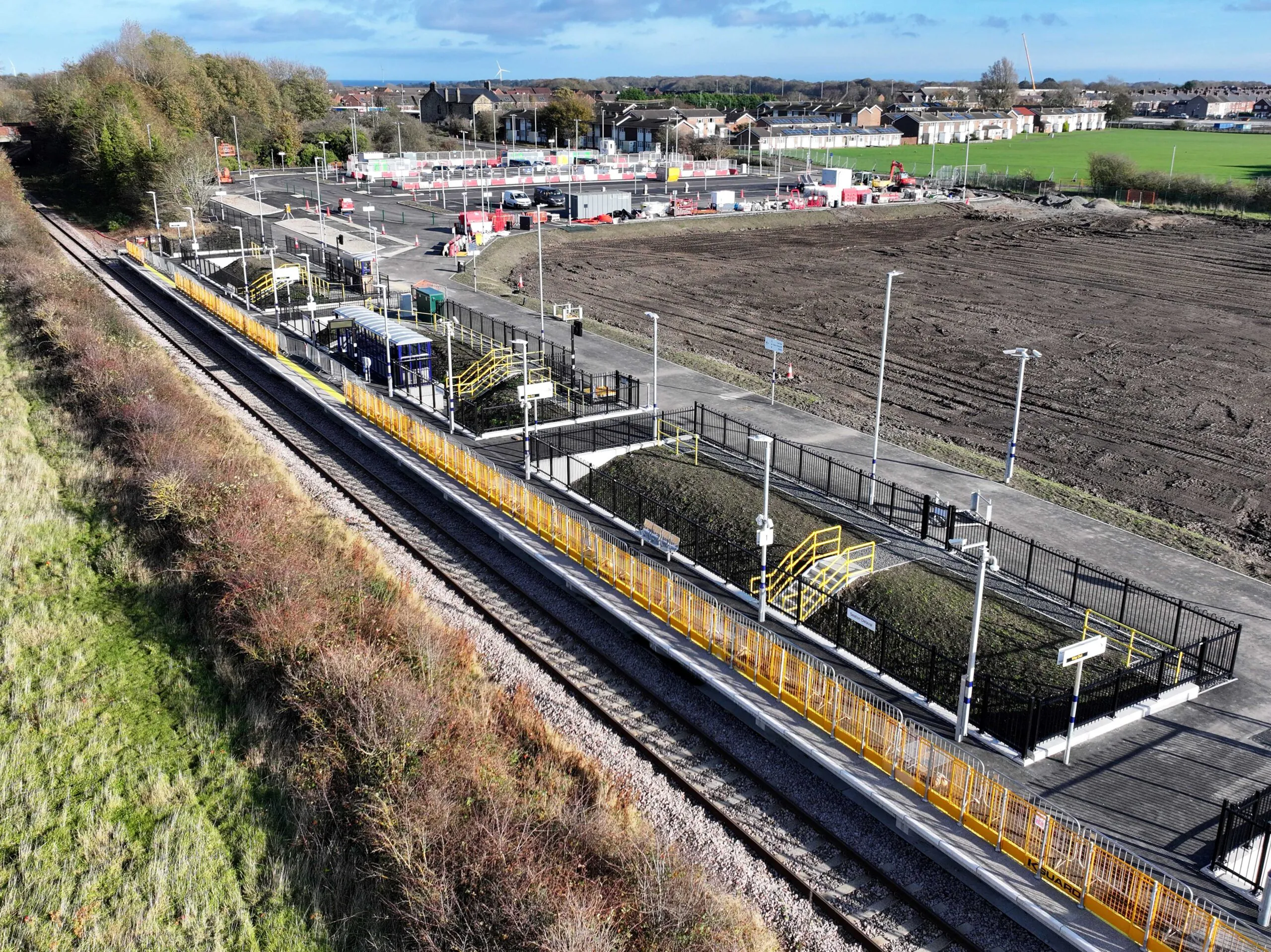 Aerial view of train station platforms and adjacent areas still under development surrounded by greenery.