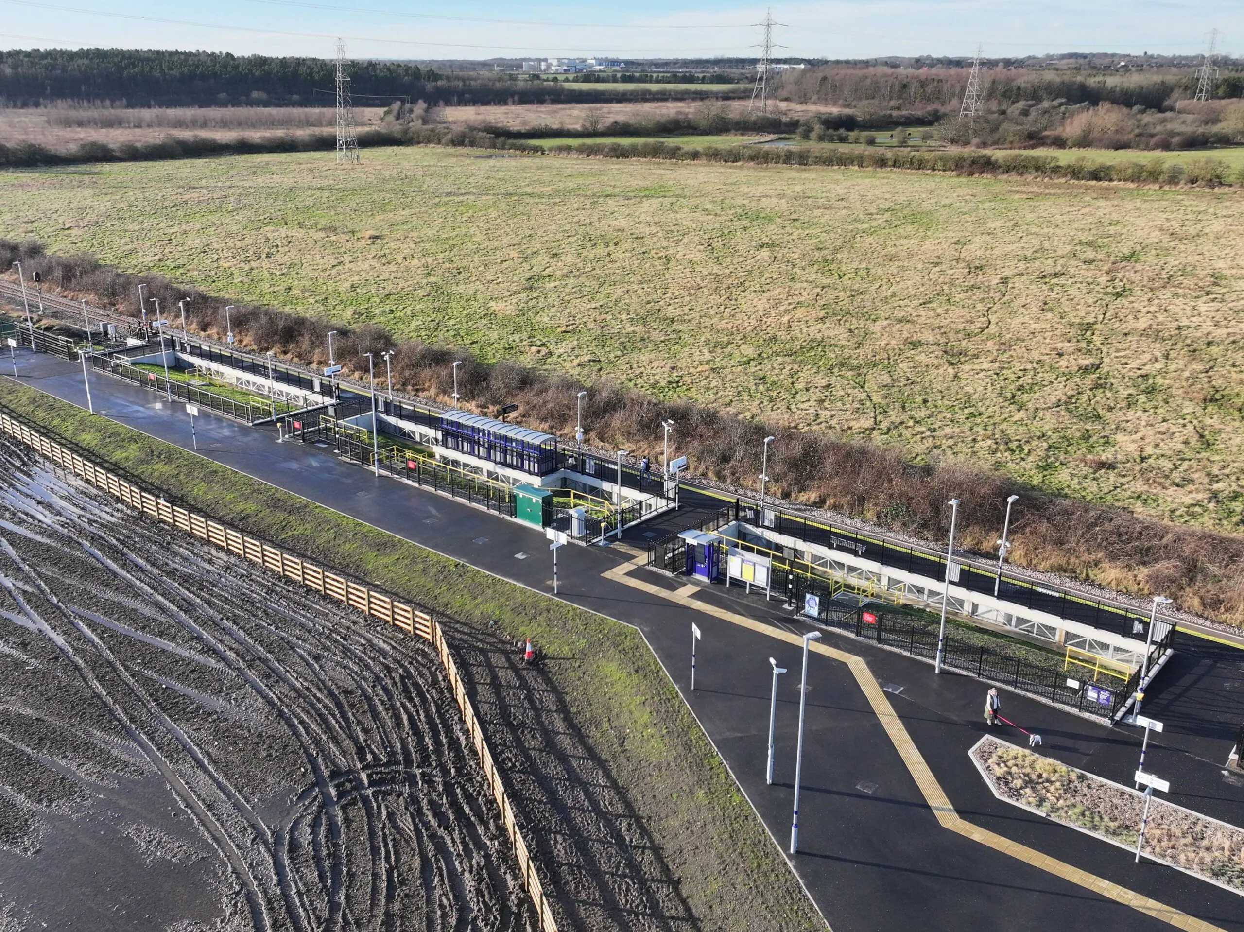 Aerial view of newly constructed train station platforms with shelters and pathways in a rural setting under clear skies.