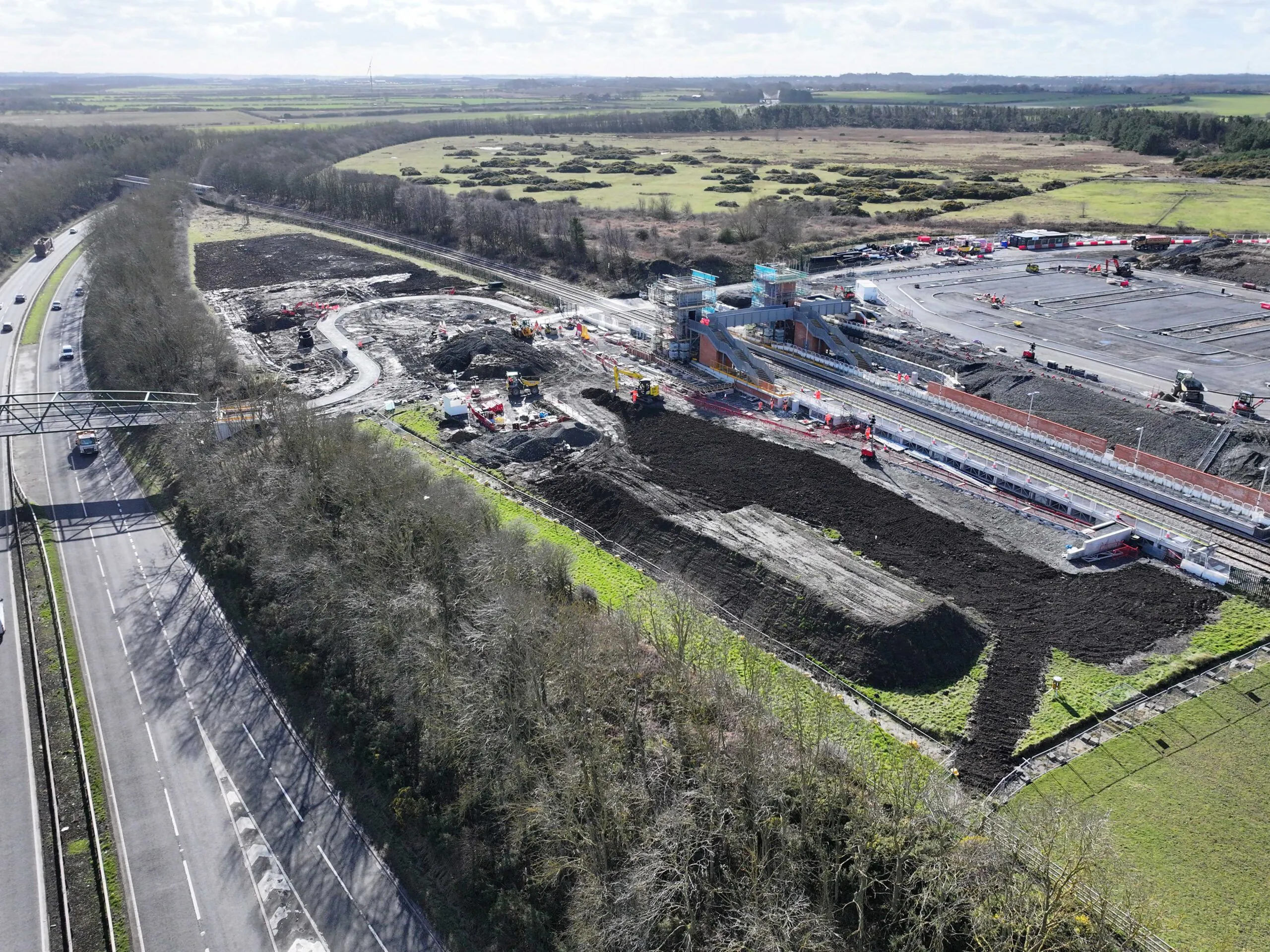 Aerial view of roadworks near open fields and highways with vehicles and equipment scattered across the site.