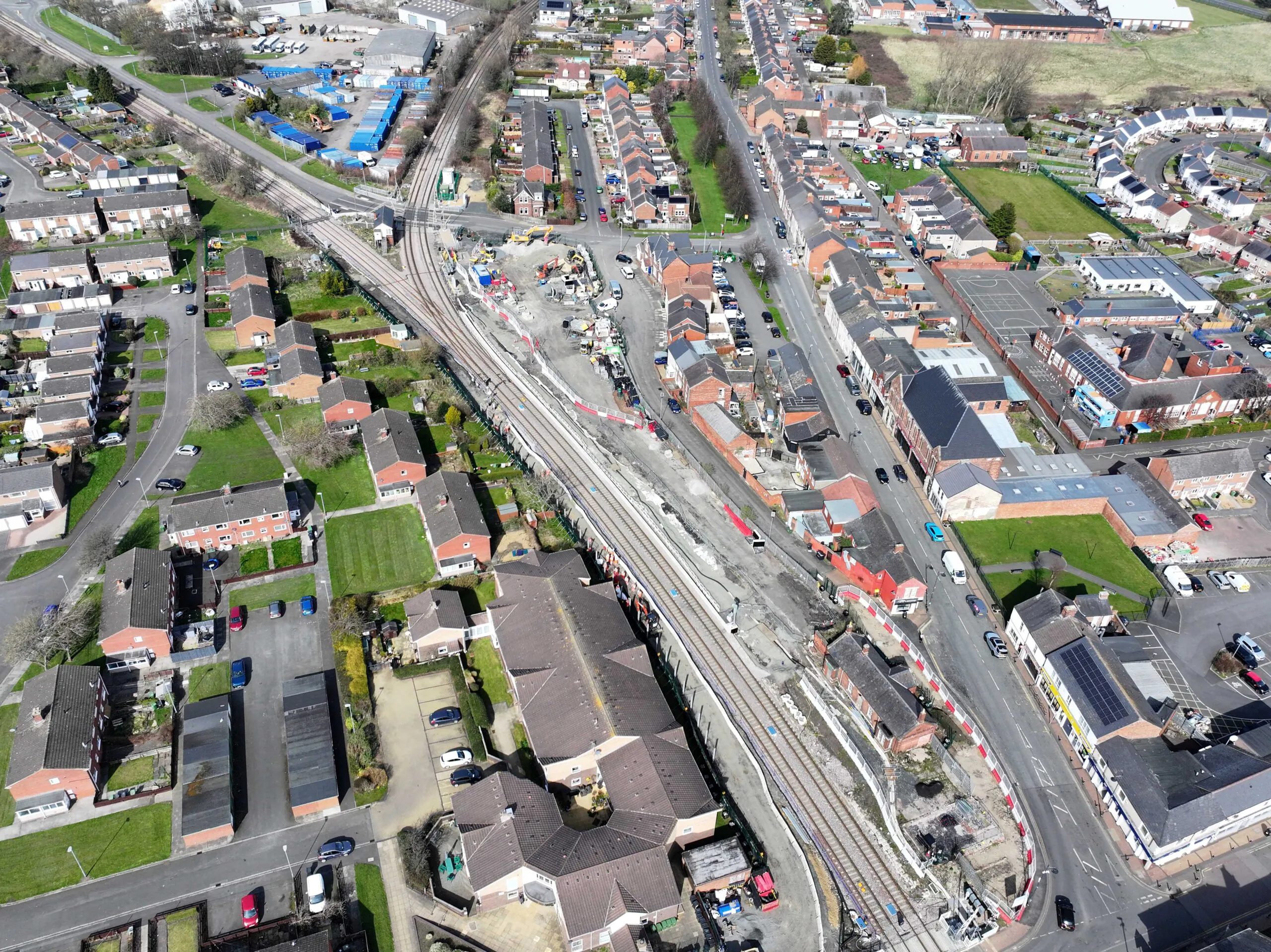 Aerial view of roadworks along railway tracks passing through a town with houses and shops nearby.