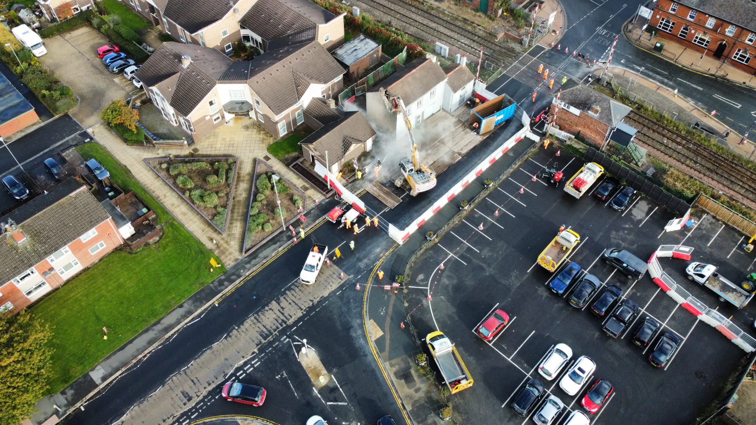 Excavator operating at a construction site near railway tracks with safety fencing and workers in high-visibility clothing.
