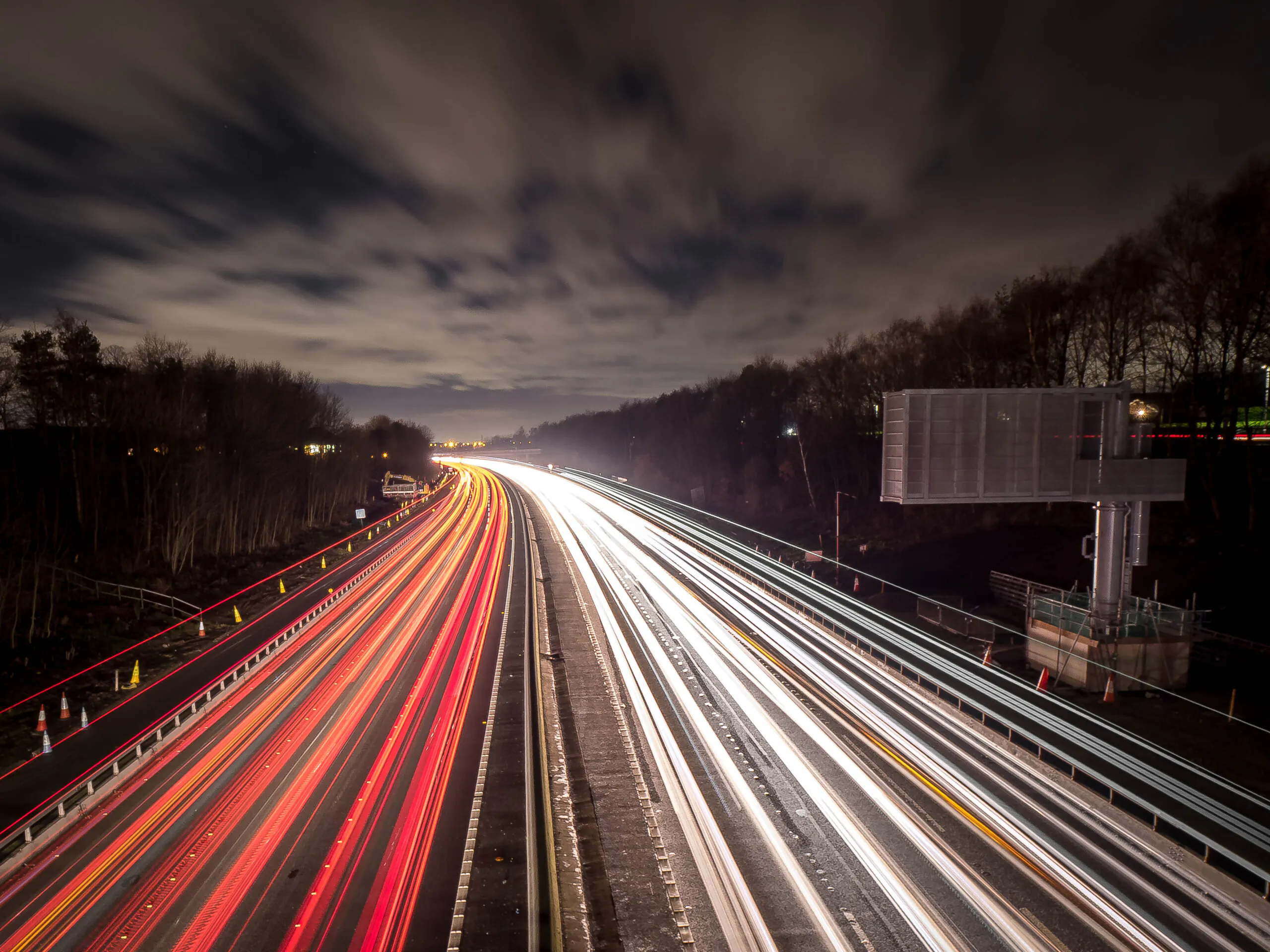 Nighttime long-exposure photo of a busy highway with light trails from vehicles and illuminated streetlights.