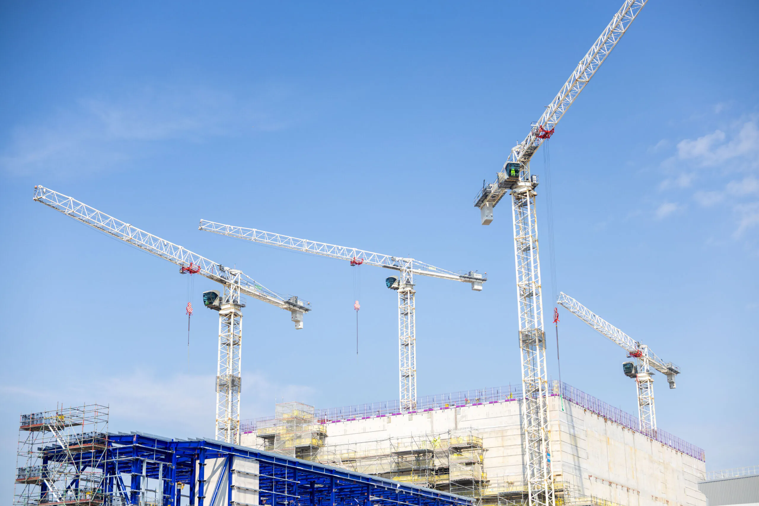 Close-up of multiple cranes assembling parts of an industrial facility against a clear blue sky.