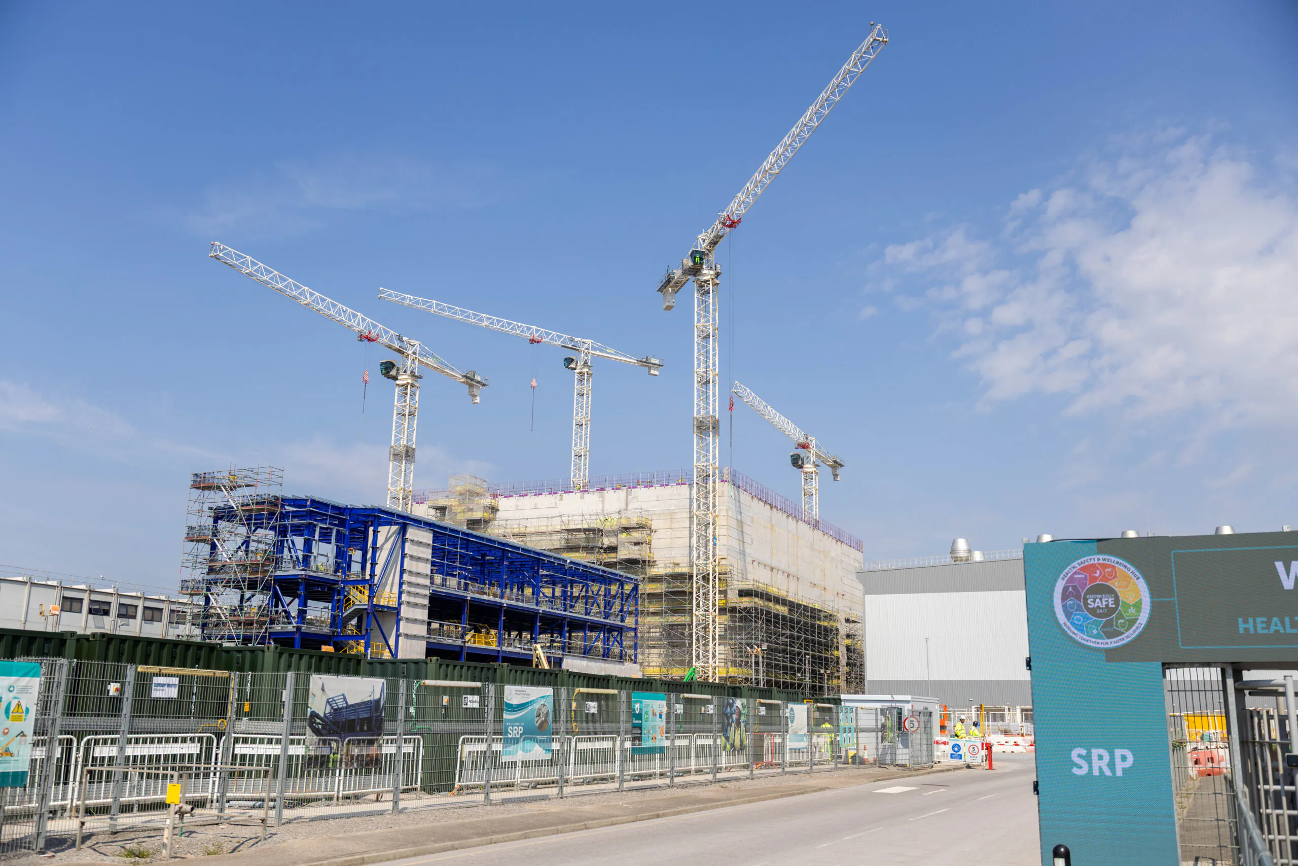 Multiple cranes surround a large building under construction, with scaffolding and fencing visible.