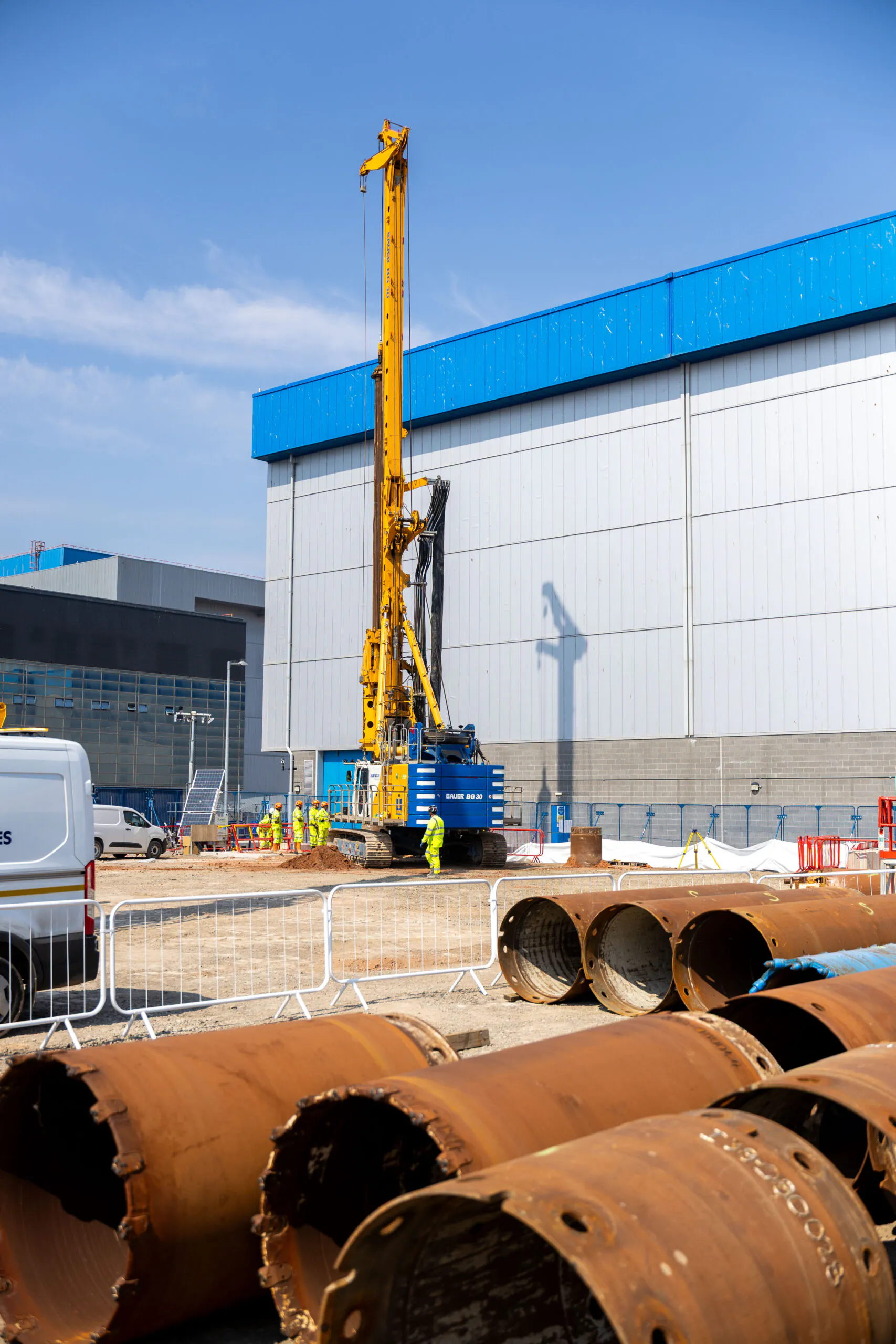 Heavy machinery and workers operate across a large construction site with various tasks underway.