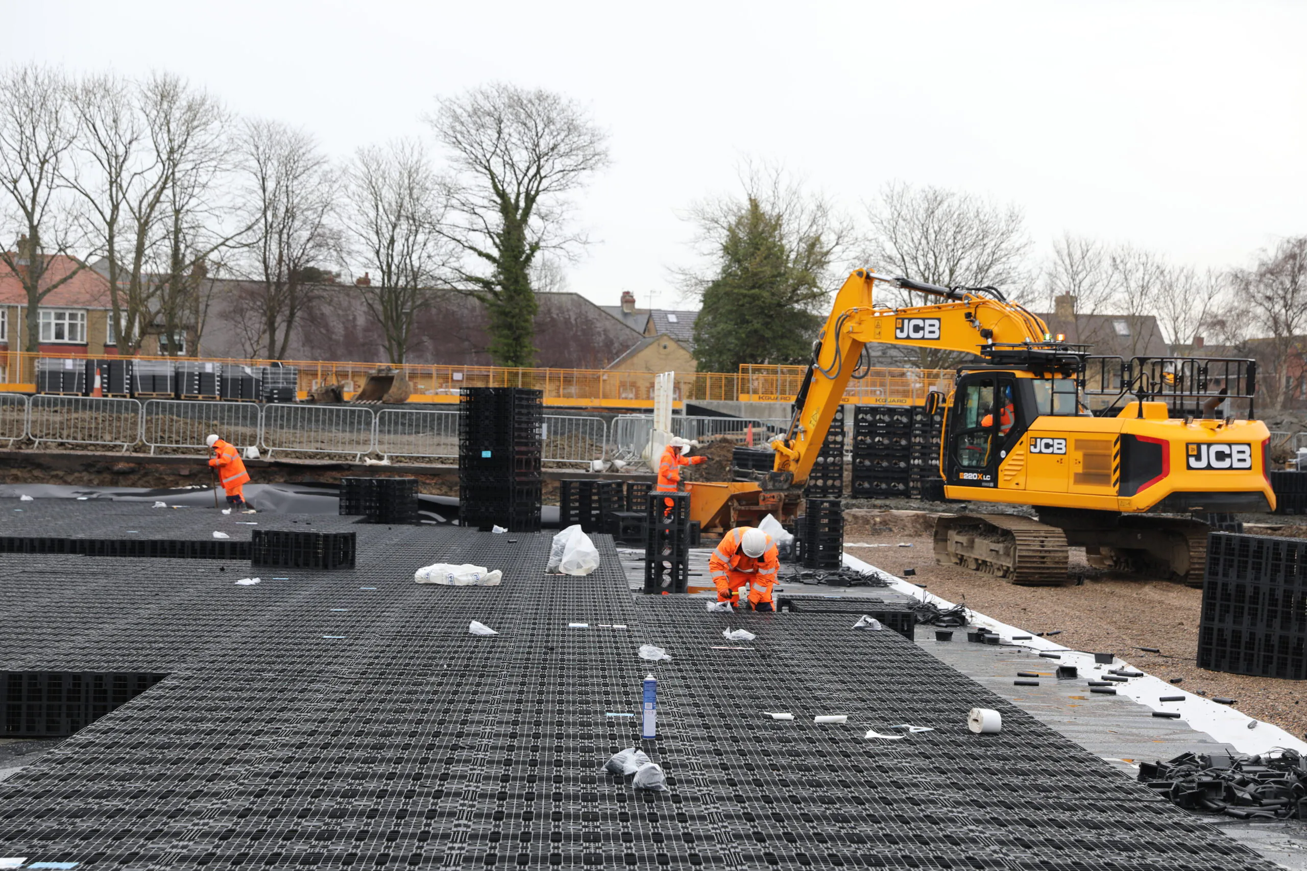 Excavator working beside railway tracks during daytime maintenance, with workers in high-visibility clothing.