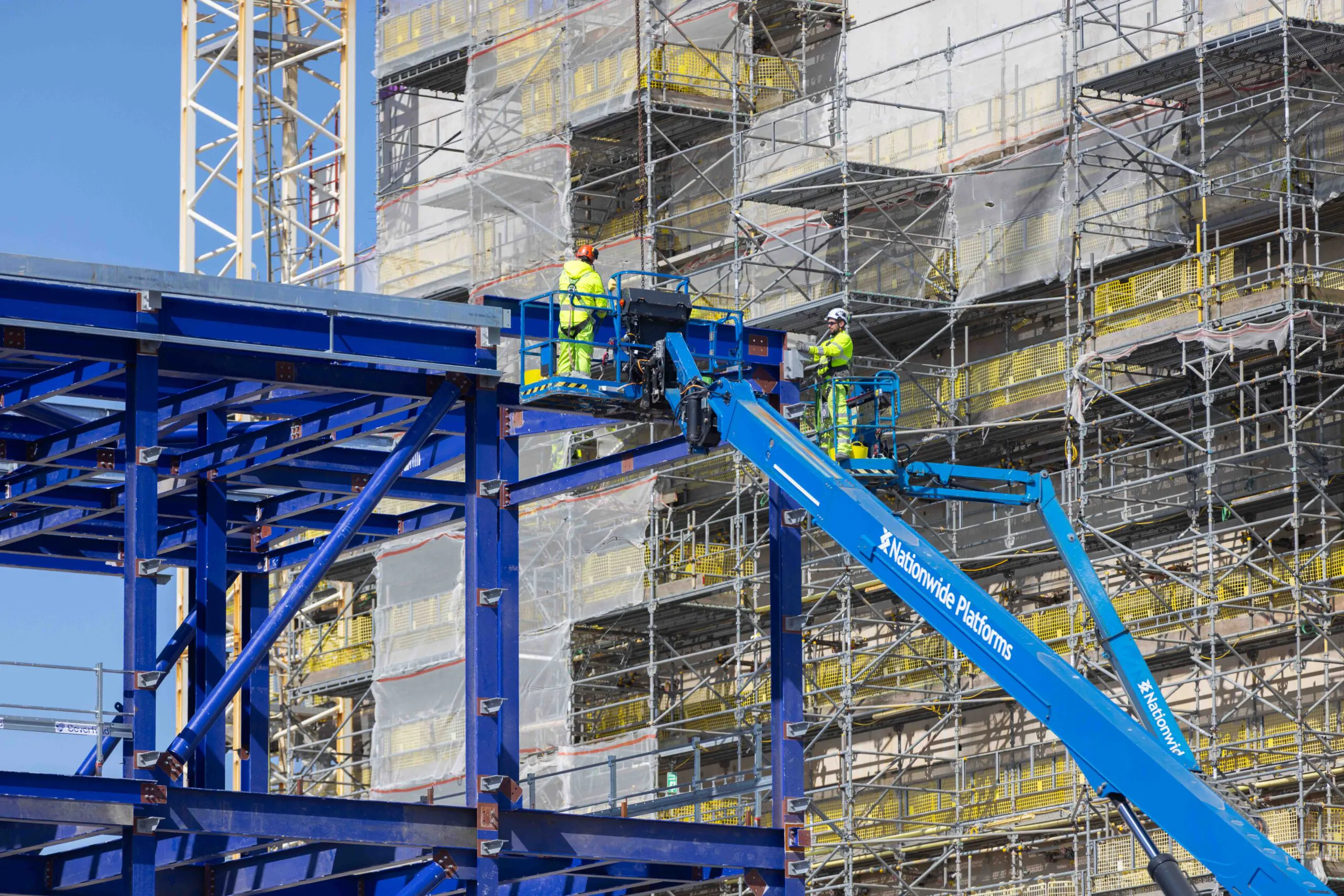 Construction worker in high-visibility gear stands near rebar and scaffolding at a large industrial site.