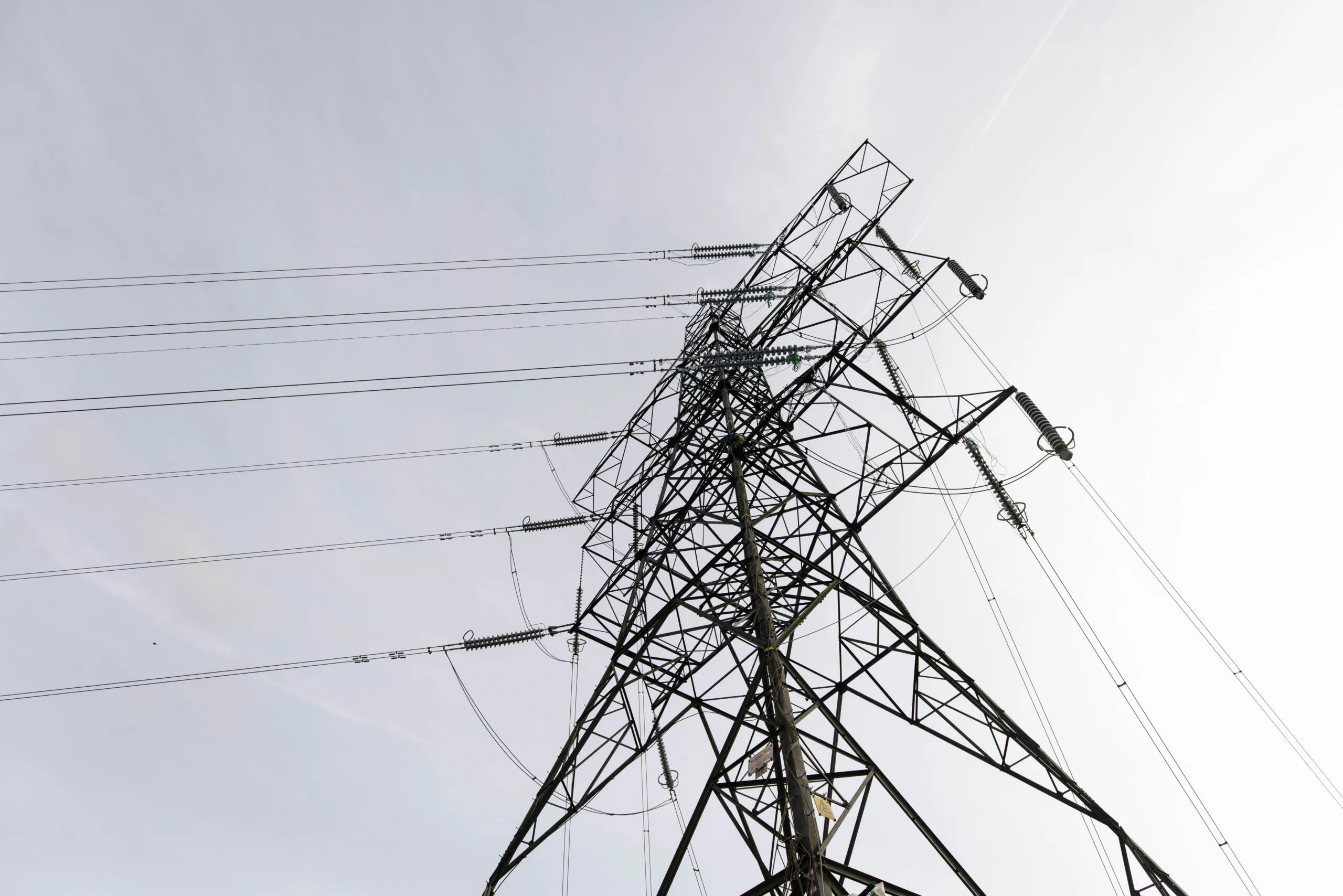 Low-angle view of workers climbing a tall metal lattice tower structure with power lines extending outward.
