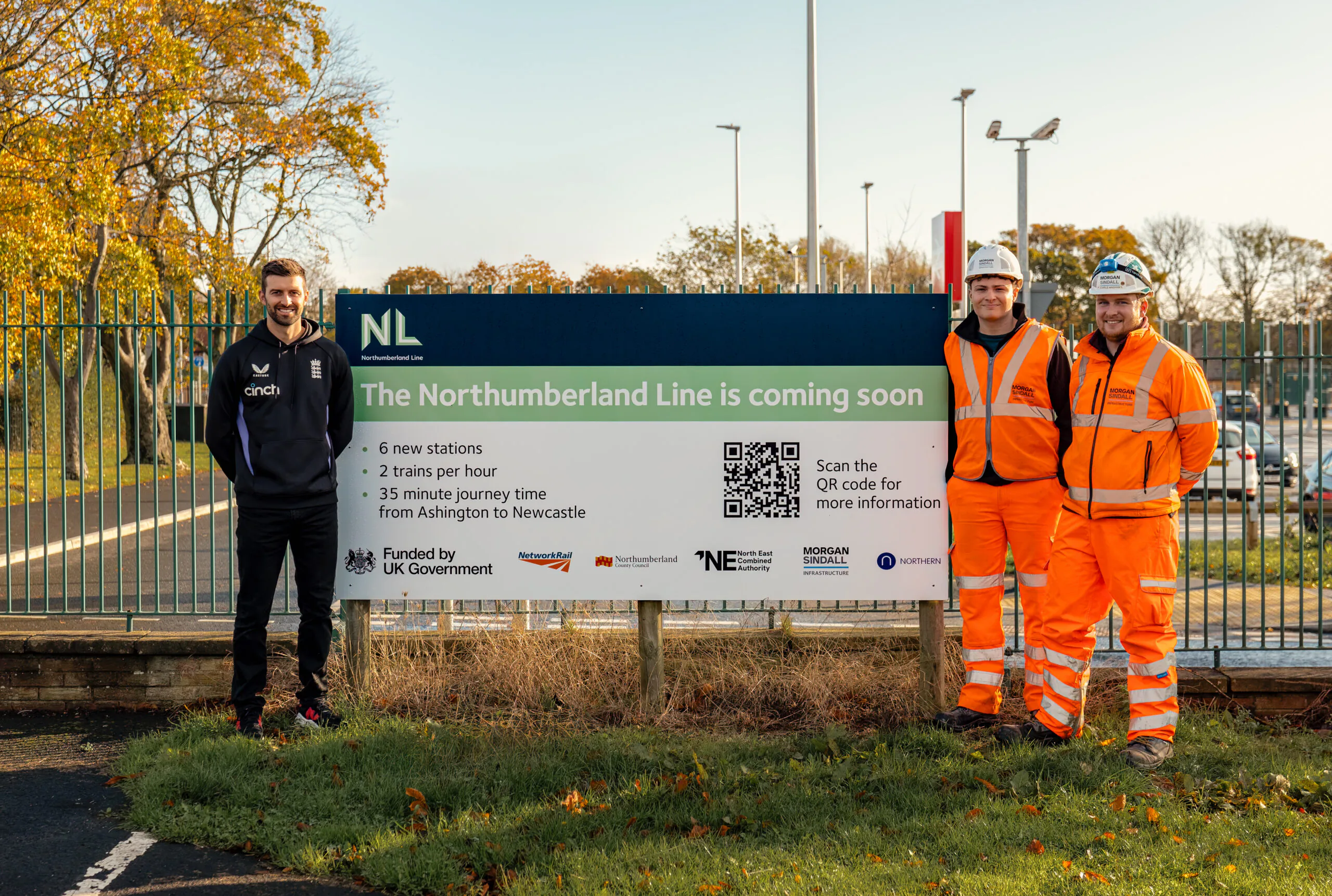 Three people standing beside a sign that reads "The Northumberland Line is coming soon," detailing six new stations, two trains per hour, and a 35-minute journey from Ashington to Newcastle.