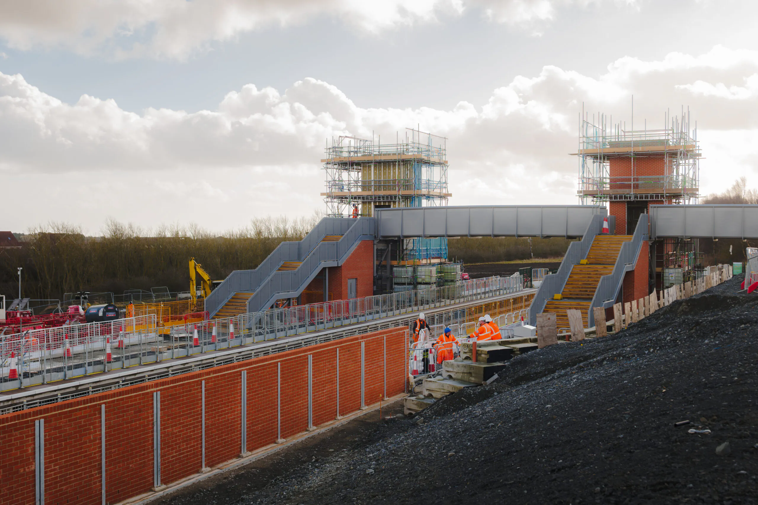 Elevated train station under construction with scaffolding around brick towers and metal walkways during daylight.