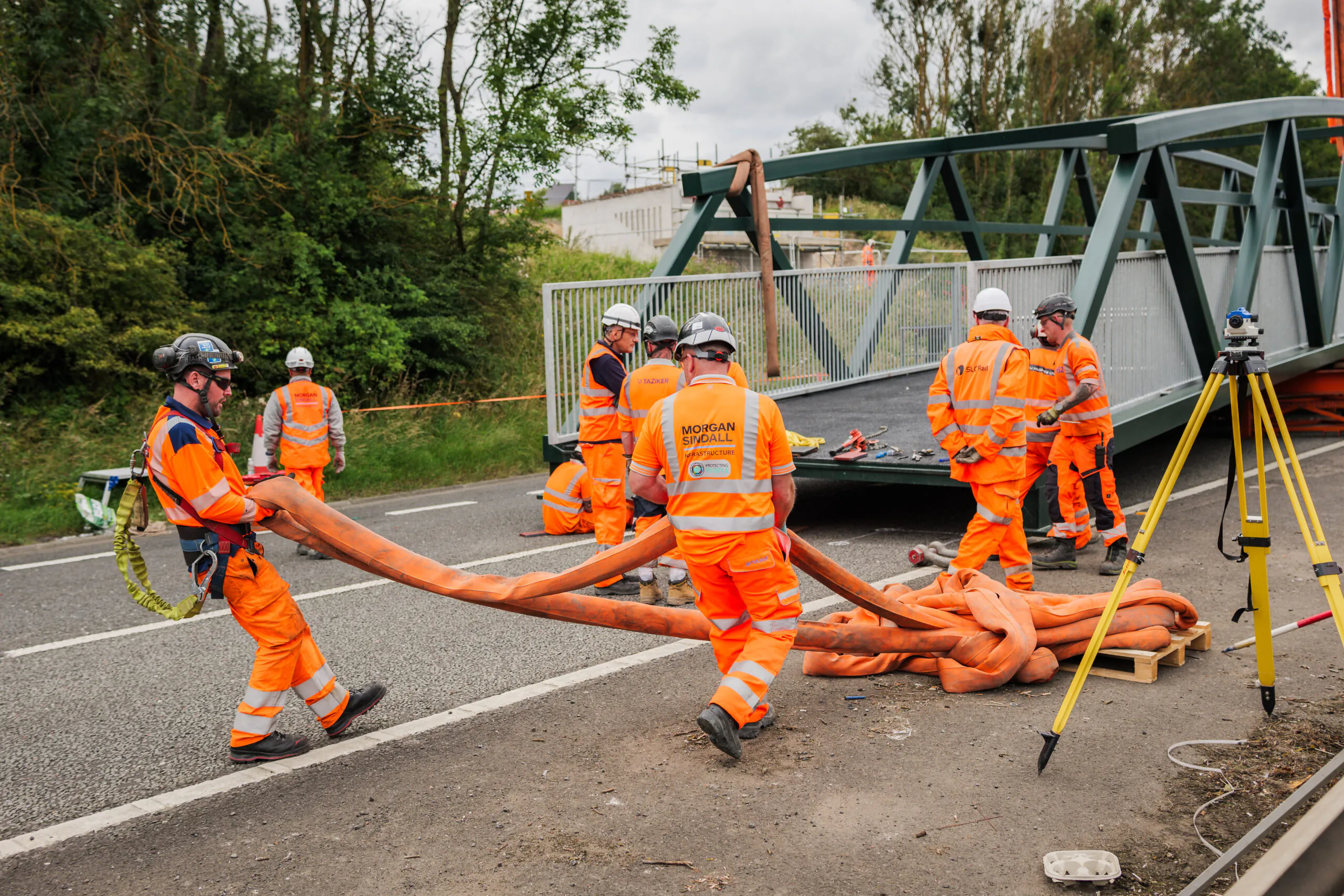 Workers assembling steel bridge components at a construction site with cranes and heavy machinery.