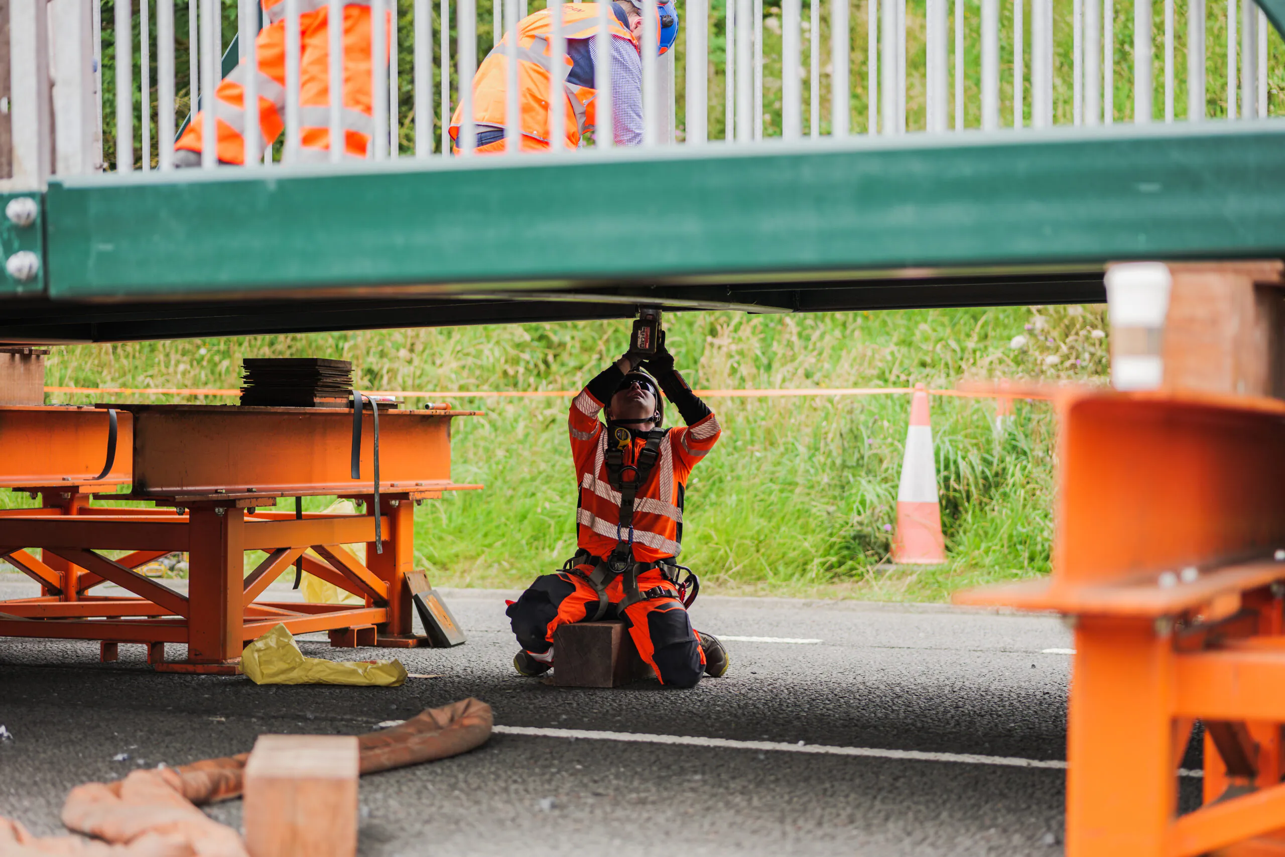 Workers installing steel beams on a bridge structure at a construction site with cranes and safety equipment.