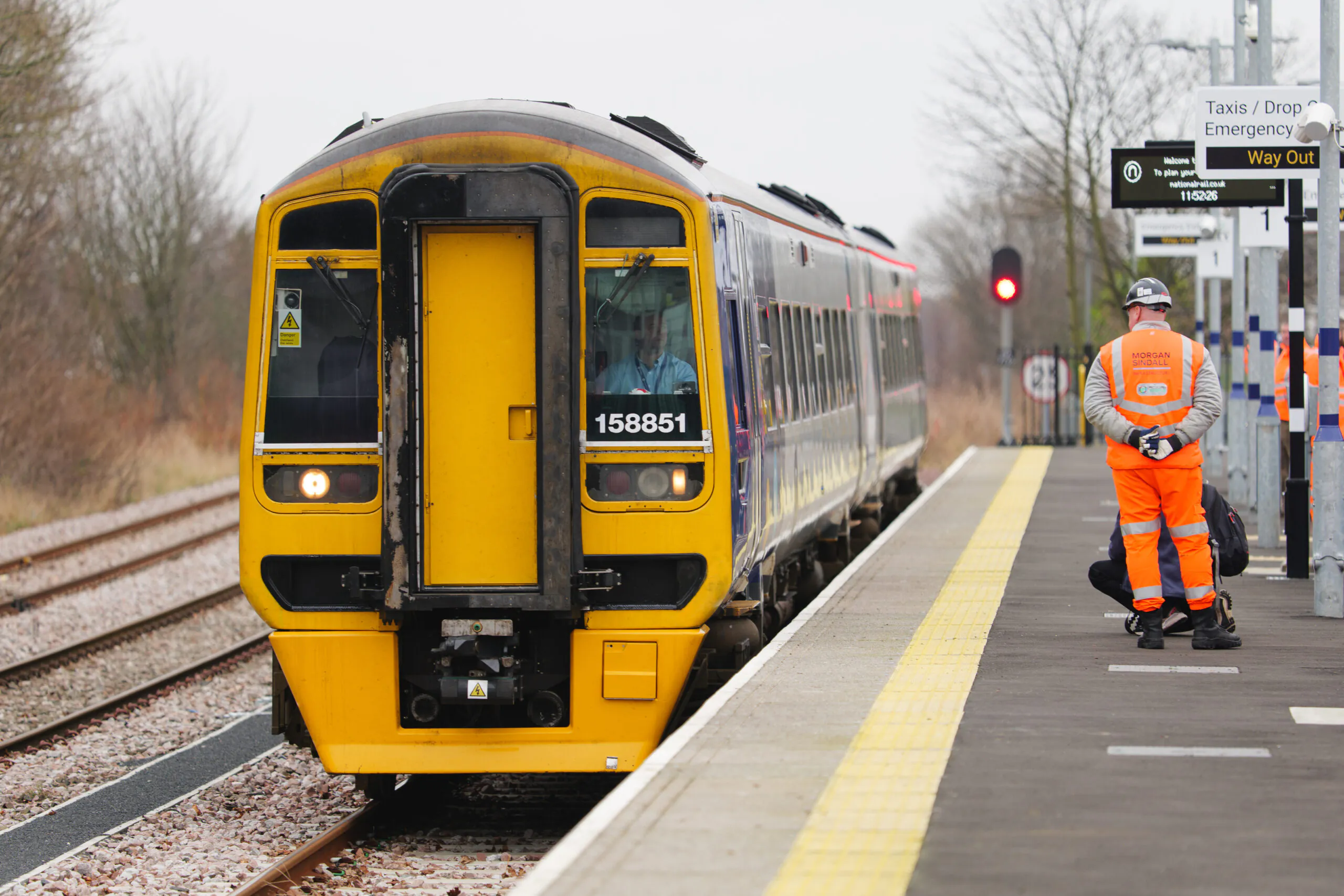 Train at a station platform with one person in high-visibility clothing standing nearby.