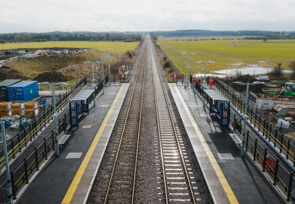 Aerial view of railway tracks flanked by platforms and fields under an overcast sky.