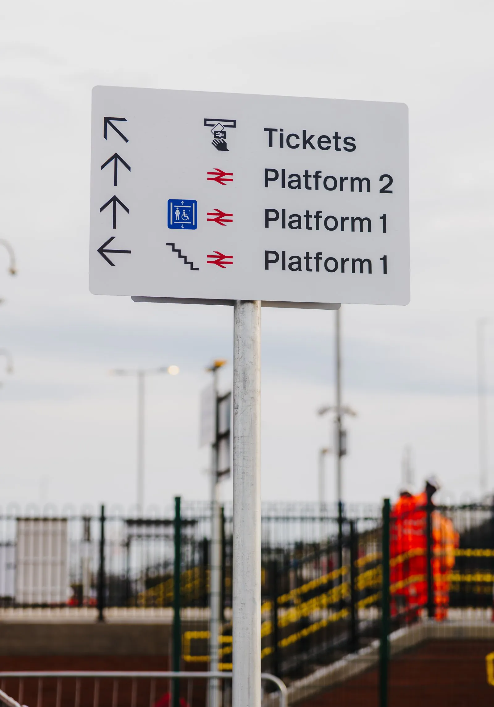Signpost showing directions to tickets, Platform 2, Platform 1, and stairs, with corresponding icons.