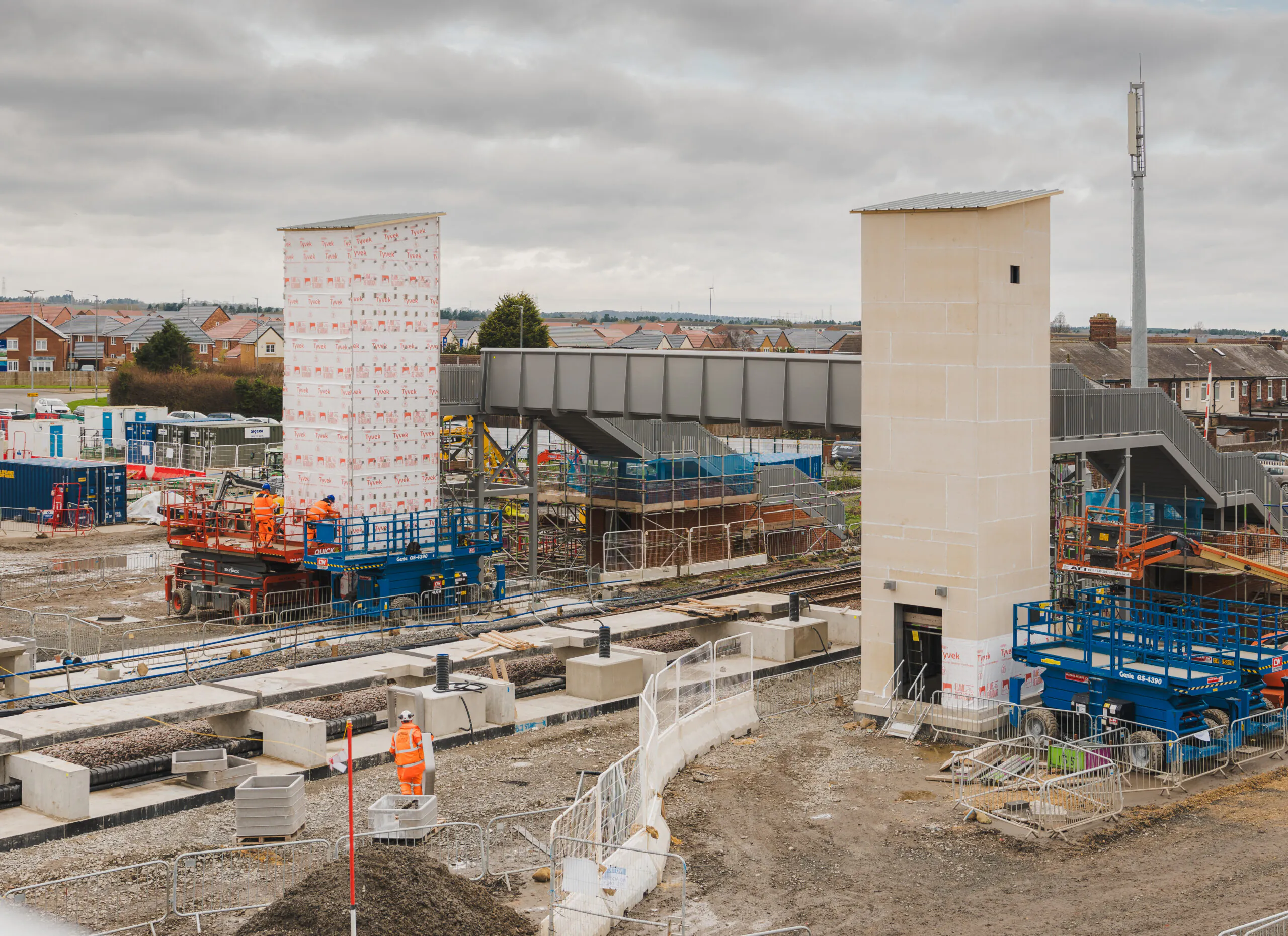 Construction site with workers assembling structural components near a railway platform.