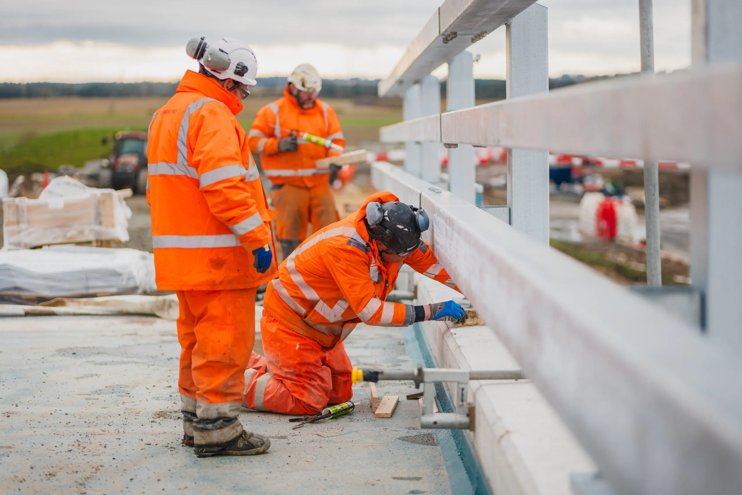 Three workers in high-visibility clothing working on a structure at a construction site during daylight.