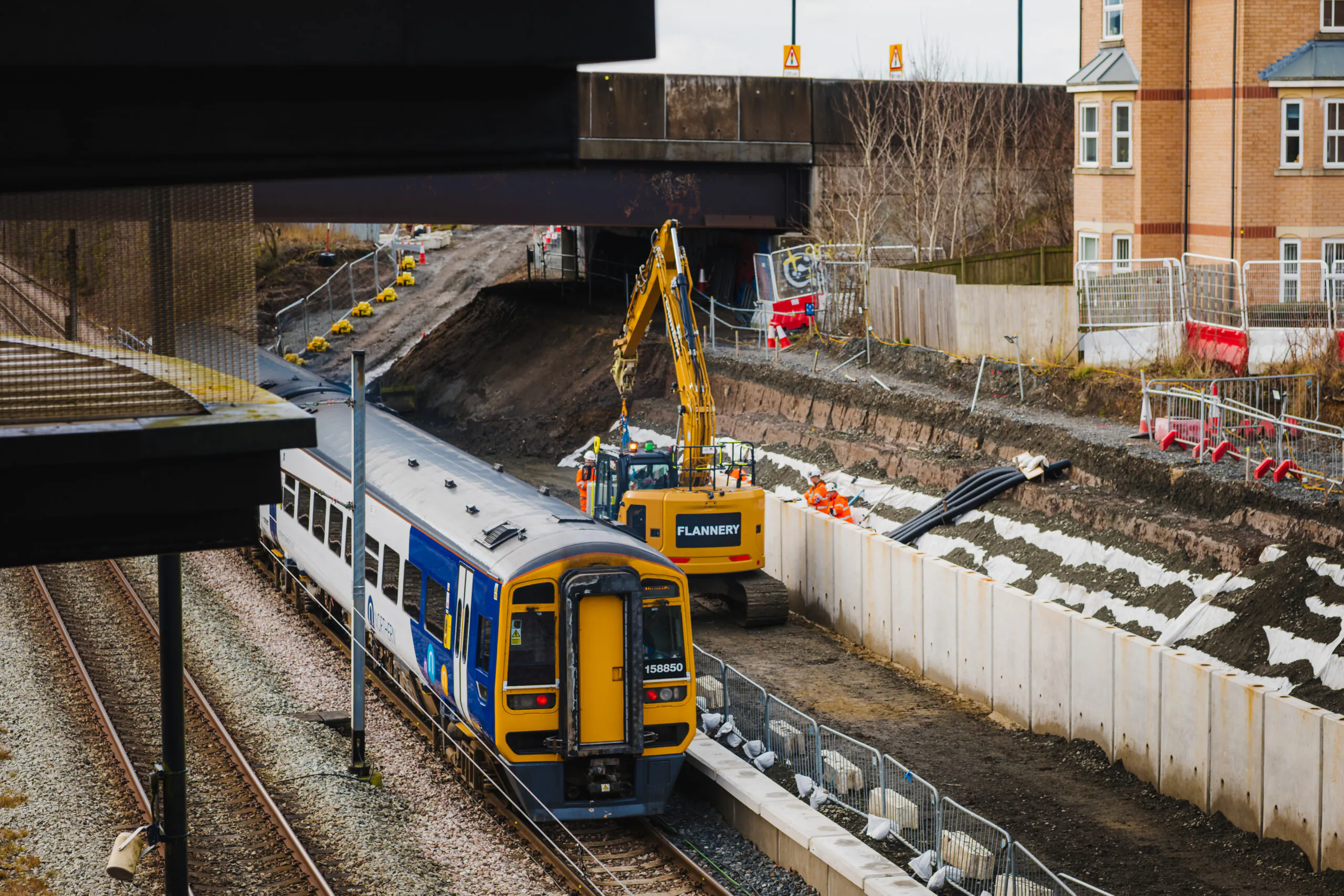 Train passing through a construction zone with workers and machinery positioned along the railway tracks.