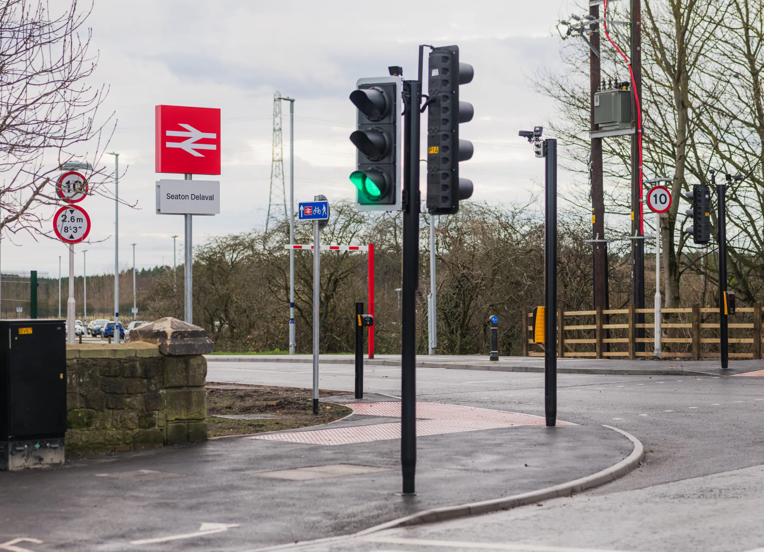 Traffic light intersection near Seaton Delaval station with speed limit and pedestrian crossing signs.