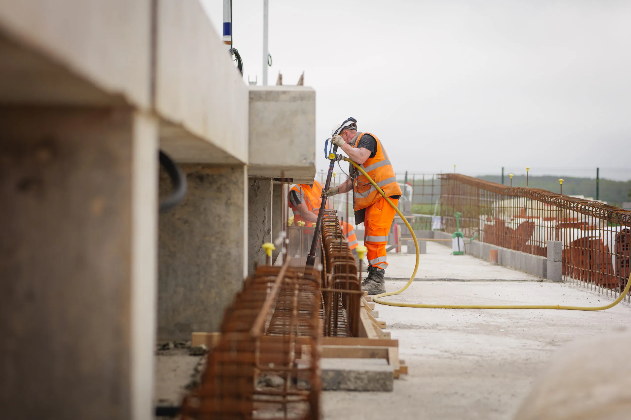 Two workers in safety gear performing tasks atop a concrete structure using specialized tools.