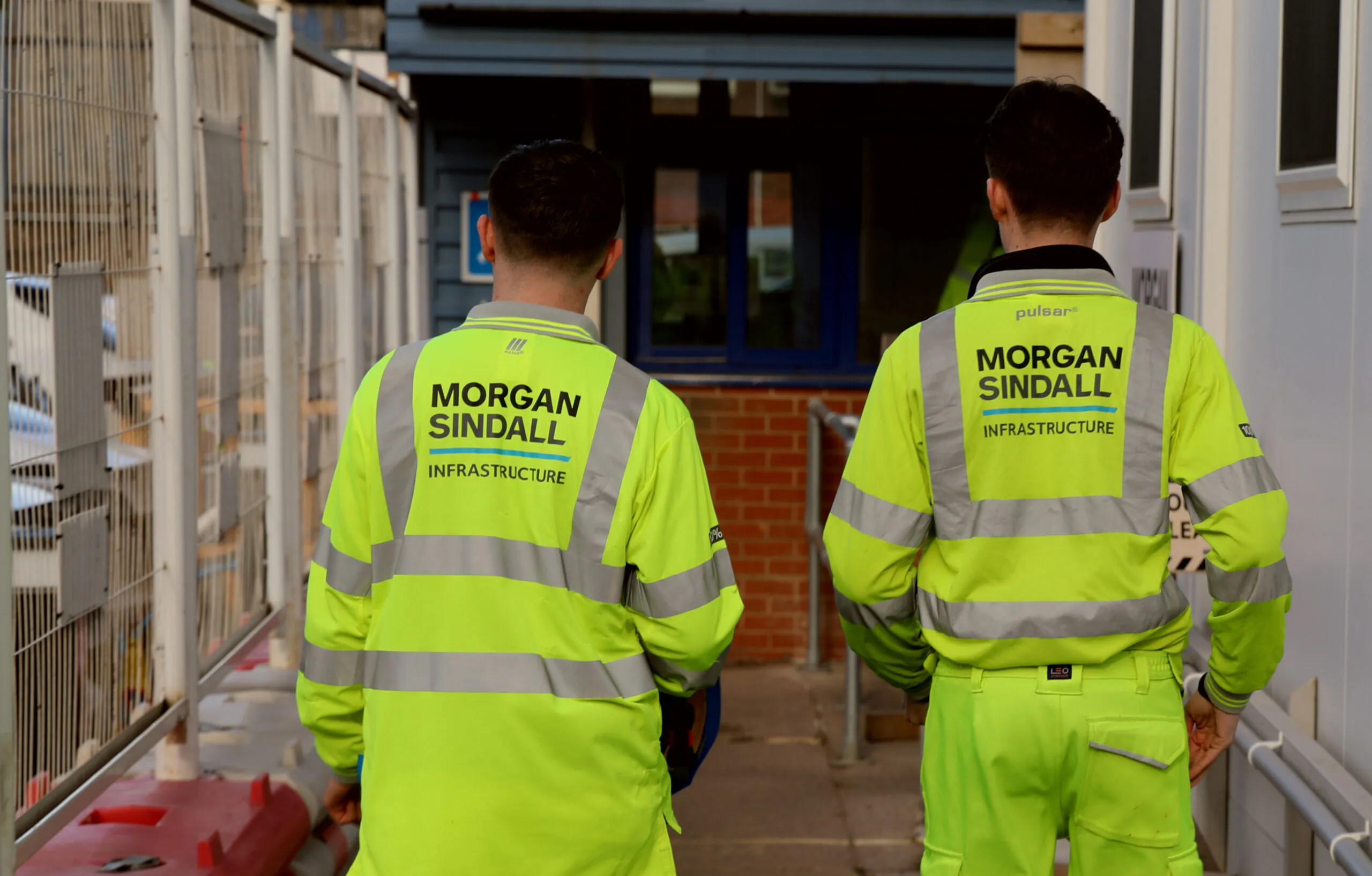 Two workers wearing Morgan Sindall Infrastructure jackets walk side by side at a construction site.