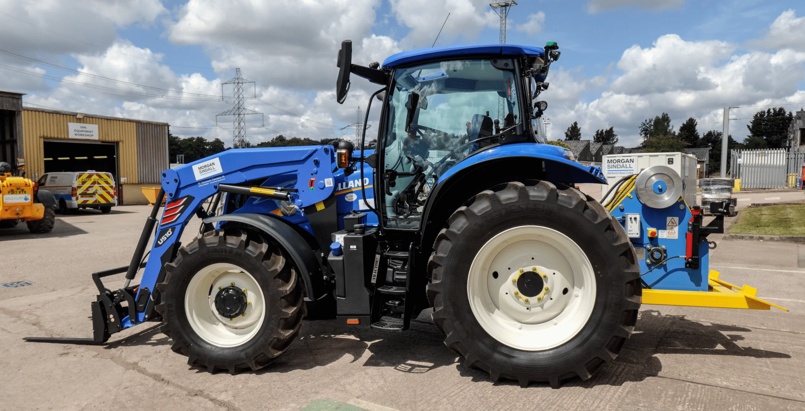 Blue tractor with winching gear branded "Townson Tractors," parked outdoors near trees and construction equipment.