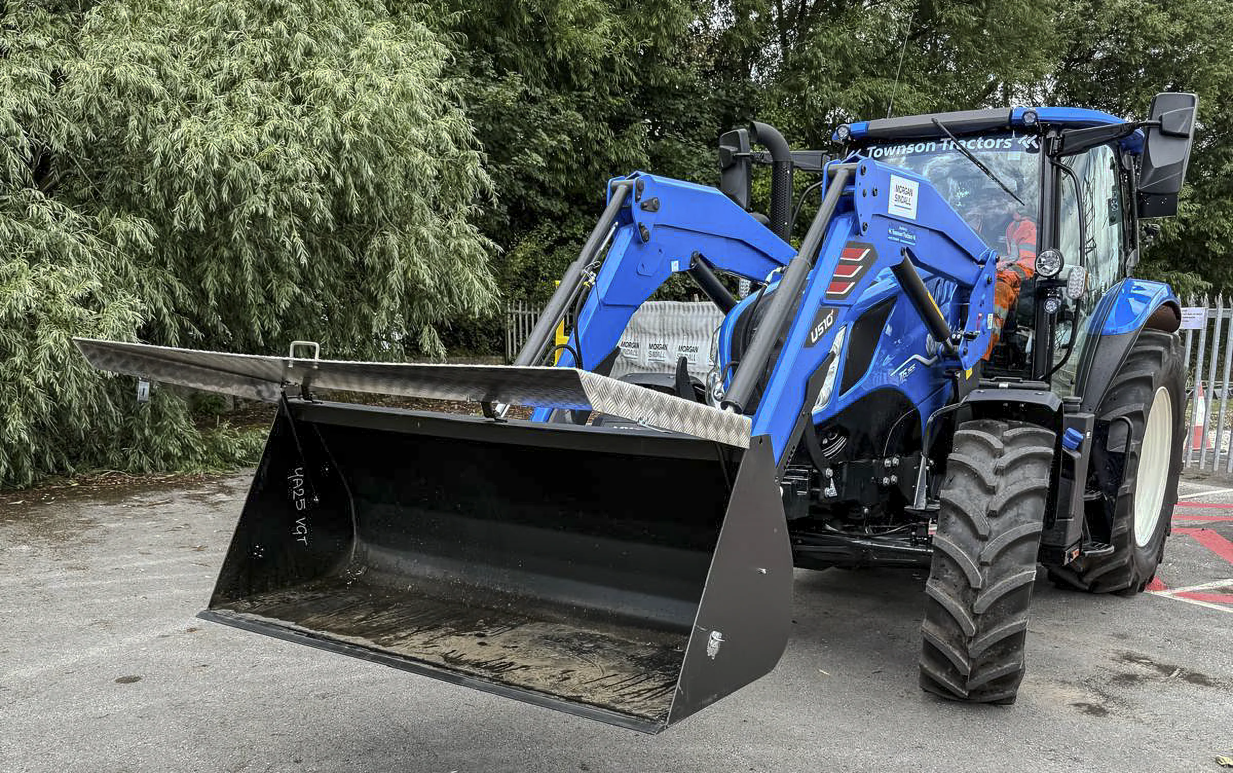 Blue tractor fitted for construction work with Townson Tractors branding, shown from the front and parked outdoors near trees.