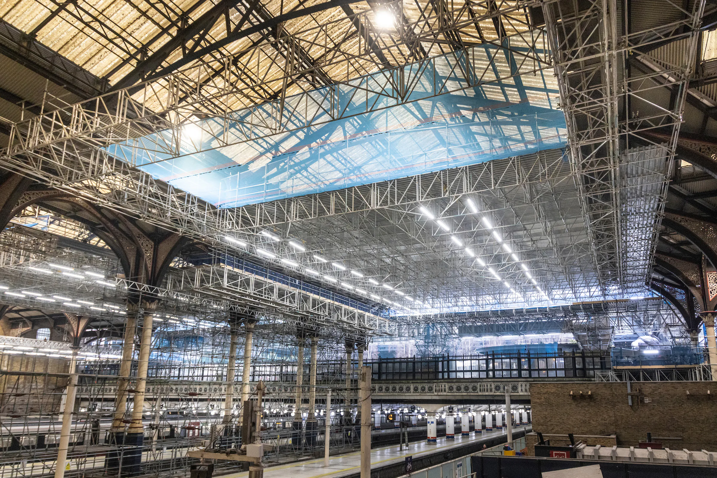 Interior of Liverpool Street Station under renovation with scaffolding supporting the ceiling and platforms.