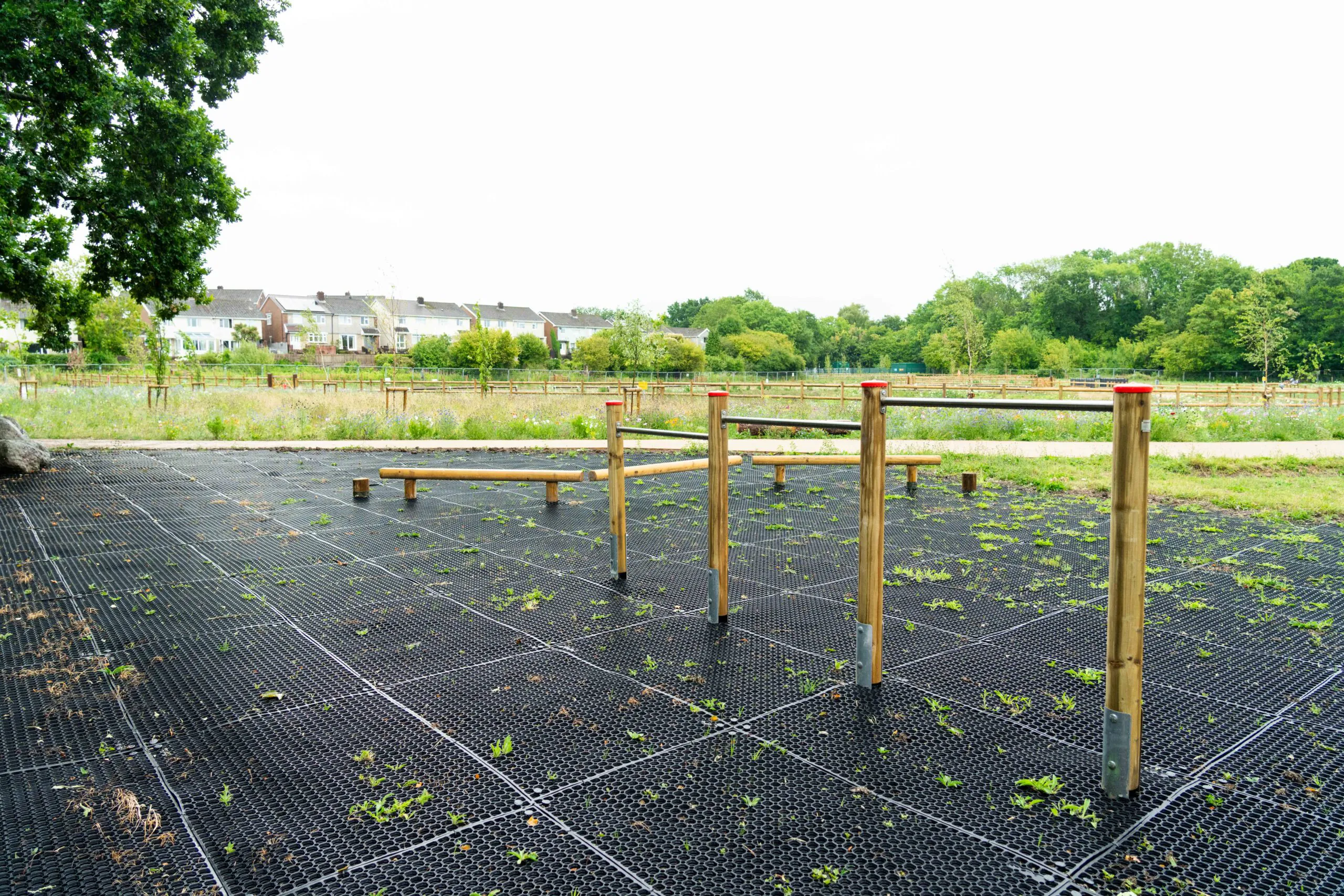 Wooden exercise bars installed on black grid flooring in an open space surrounded by grasslands and houses.