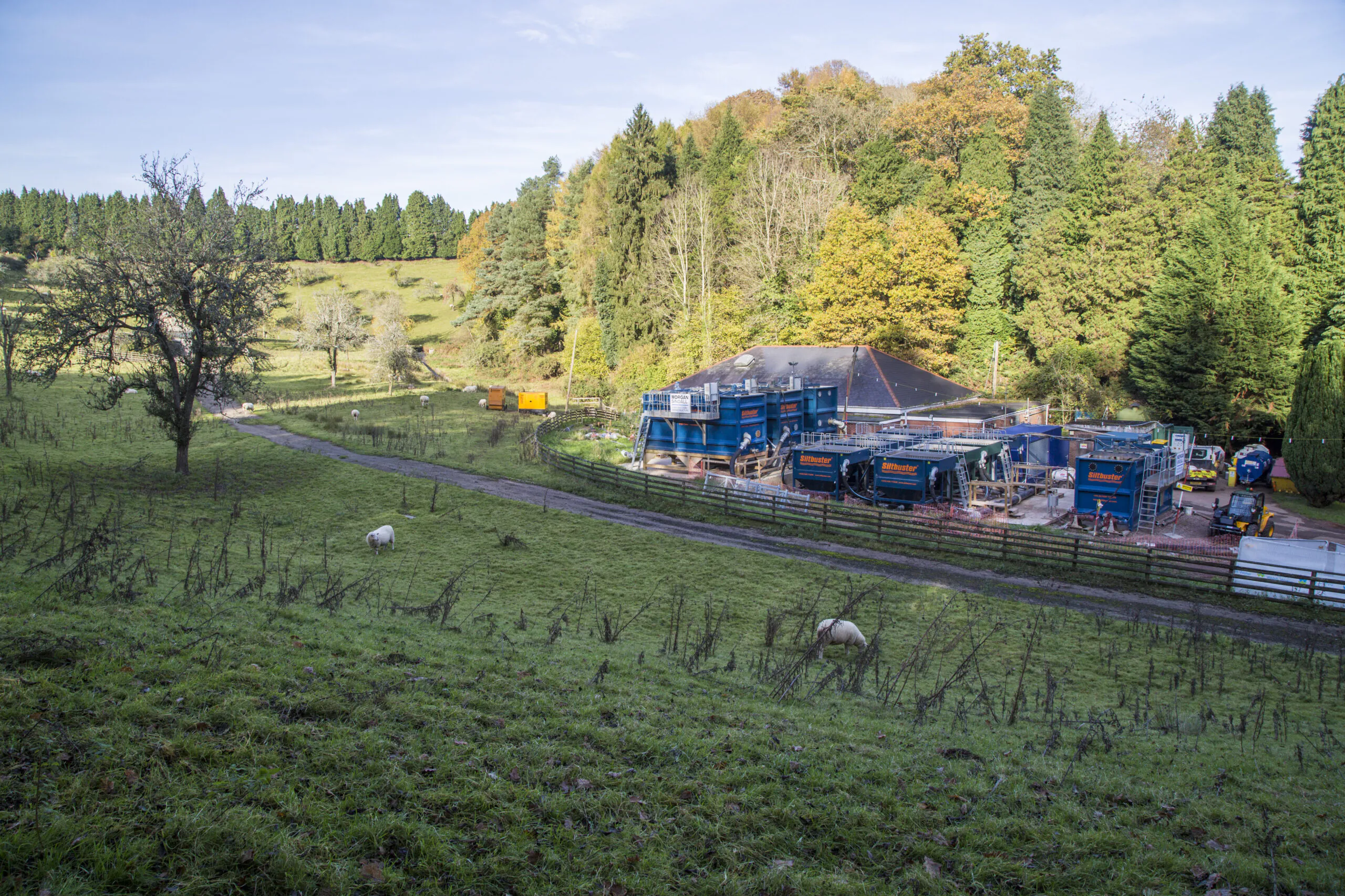 Wide view of a rural construction site with portable buildings, equipment, and surrounding green landscape.