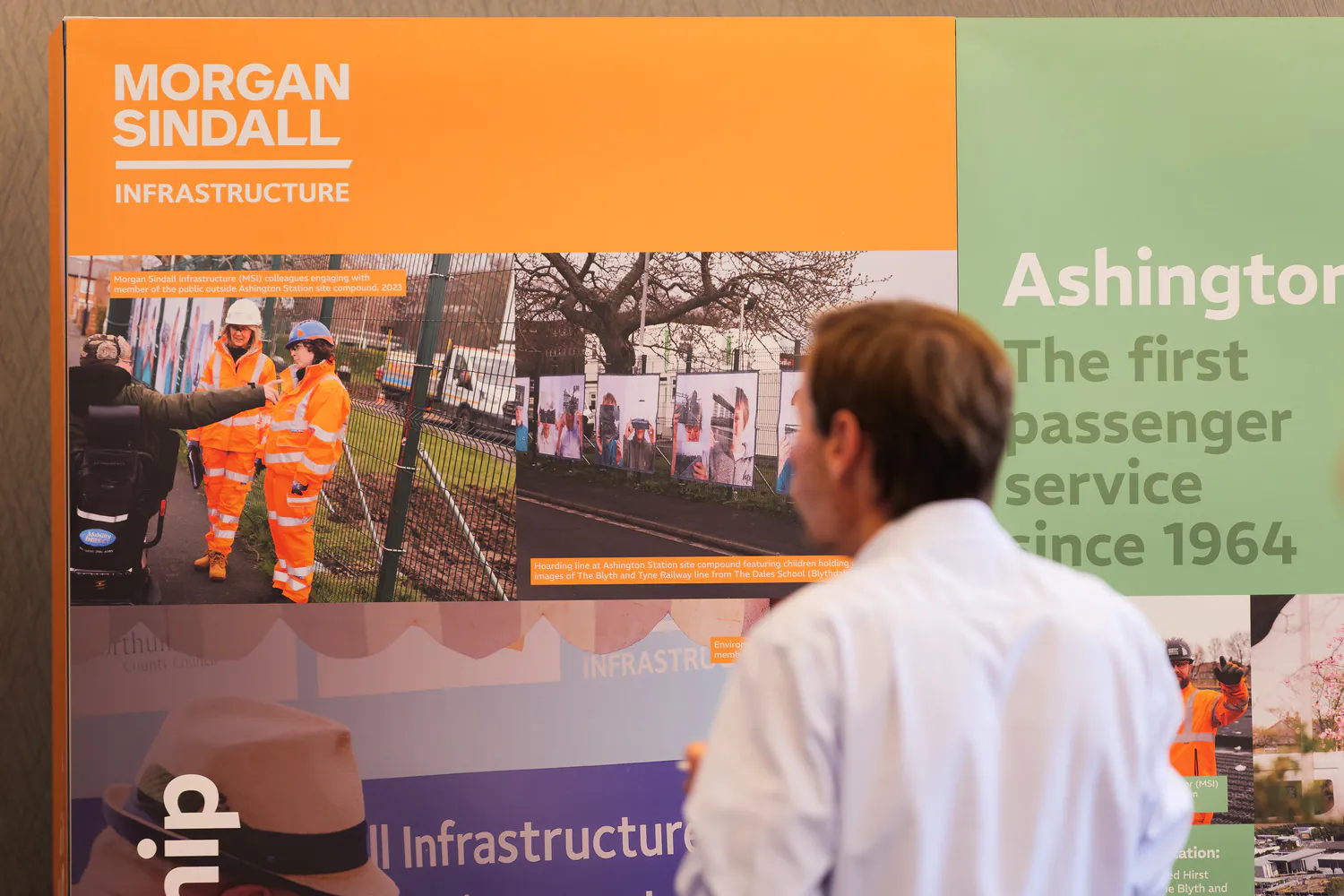 Person viewing an informational display board titled "Morgan Sindall Infrastructure," featuring images of workers in orange safety gear and project details.