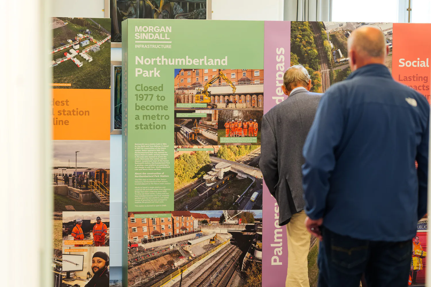 Two people examining multiple display boards about Morgan Sindall Infrastructure projects, including one titled "Northumberland Park," with images and historical information.