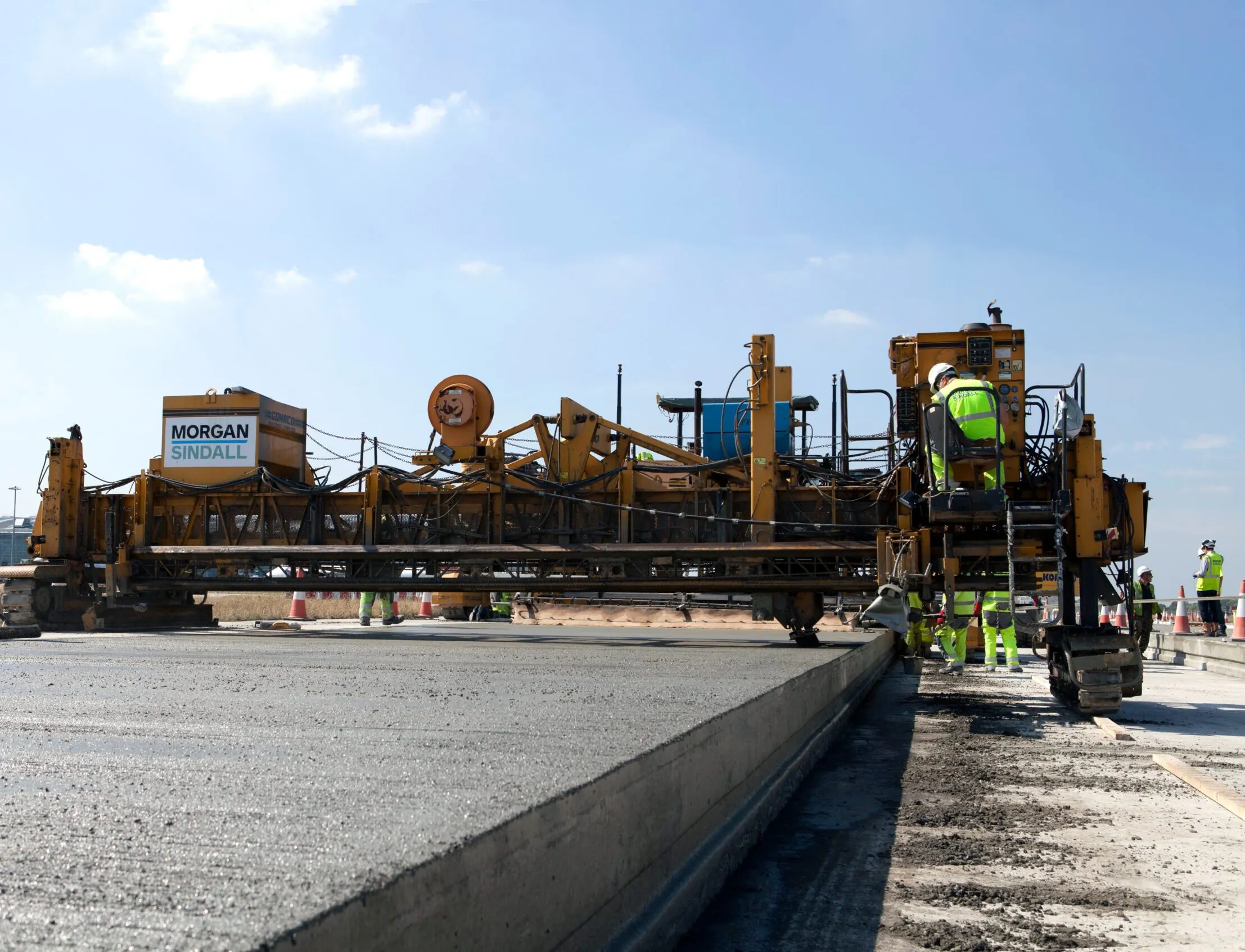 Close-up of Morgan Sindall construction machine actively paving concrete with workers surrounding it.