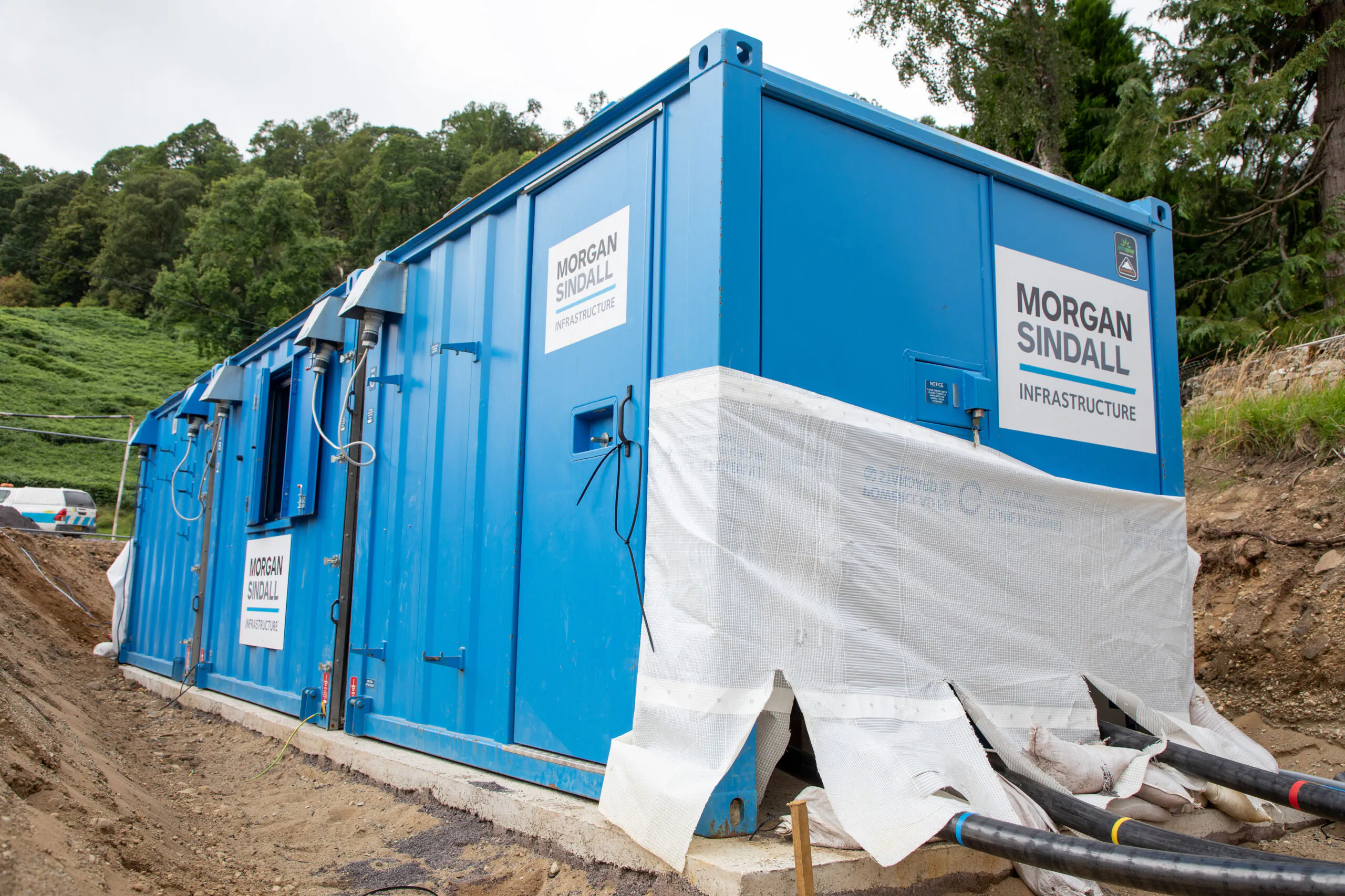 Large blue container labeled "Morgan Sindall Infrastructure" partially covered with protective material at a construction site.