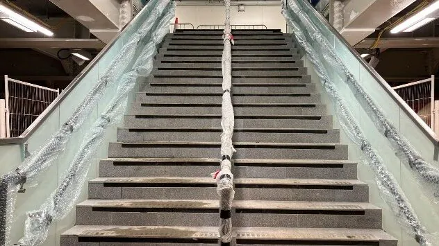Interior view of a staircase under construction with wrapped handrails and unfinished steps in a public infrastructure setting.