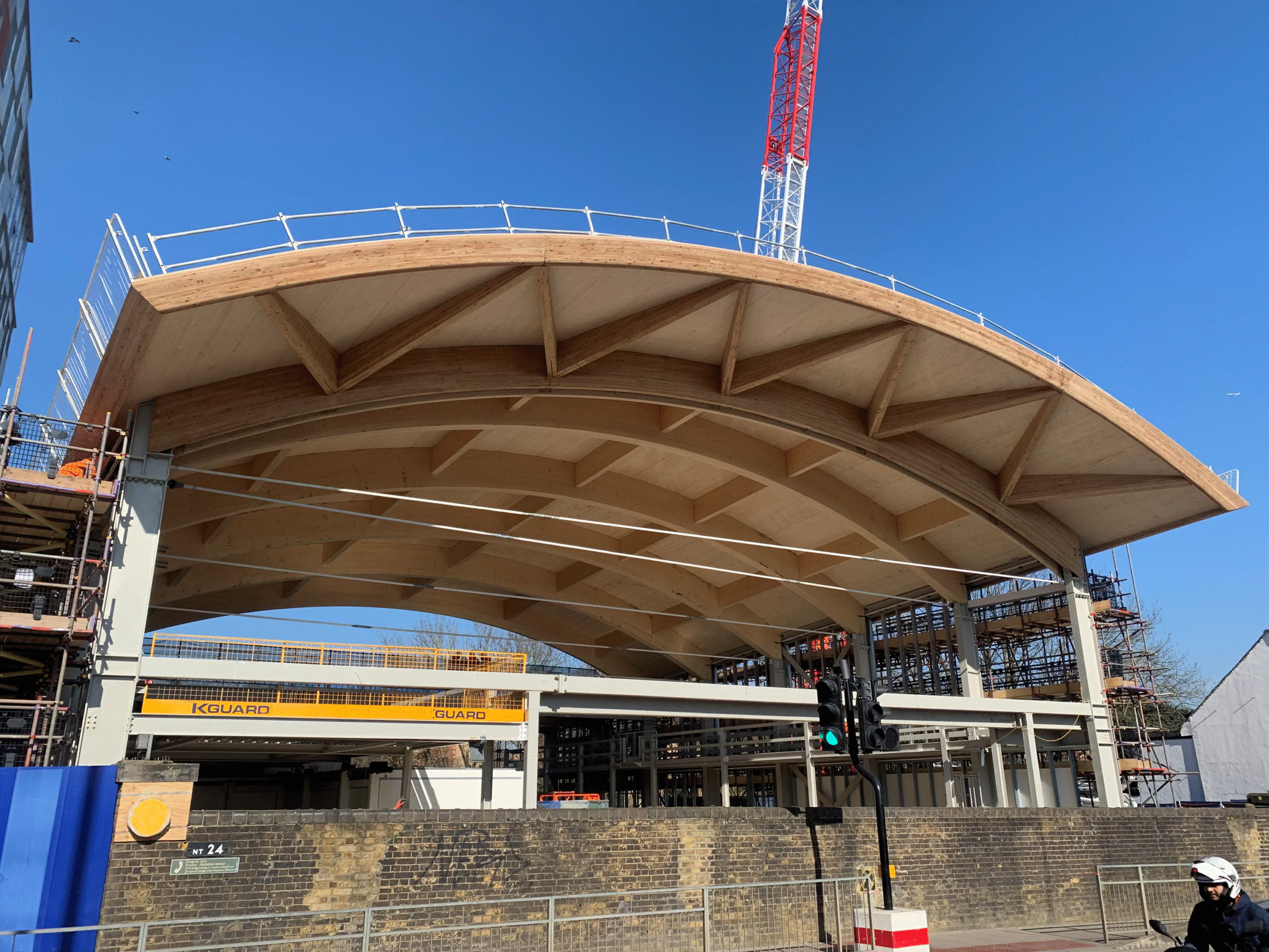 Construction progress at Colindale Station showing wooden roof structure, scaffolding, and signage.