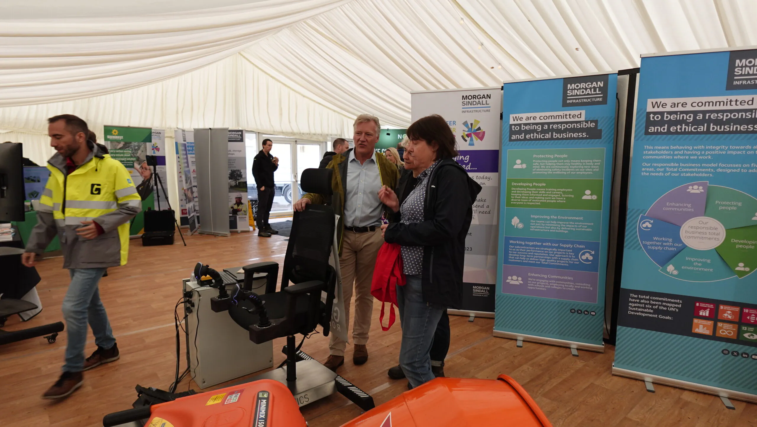Inside an exhibition tent, people interact around booths showcasing products and services related to Morgan Sindall infrastructure.