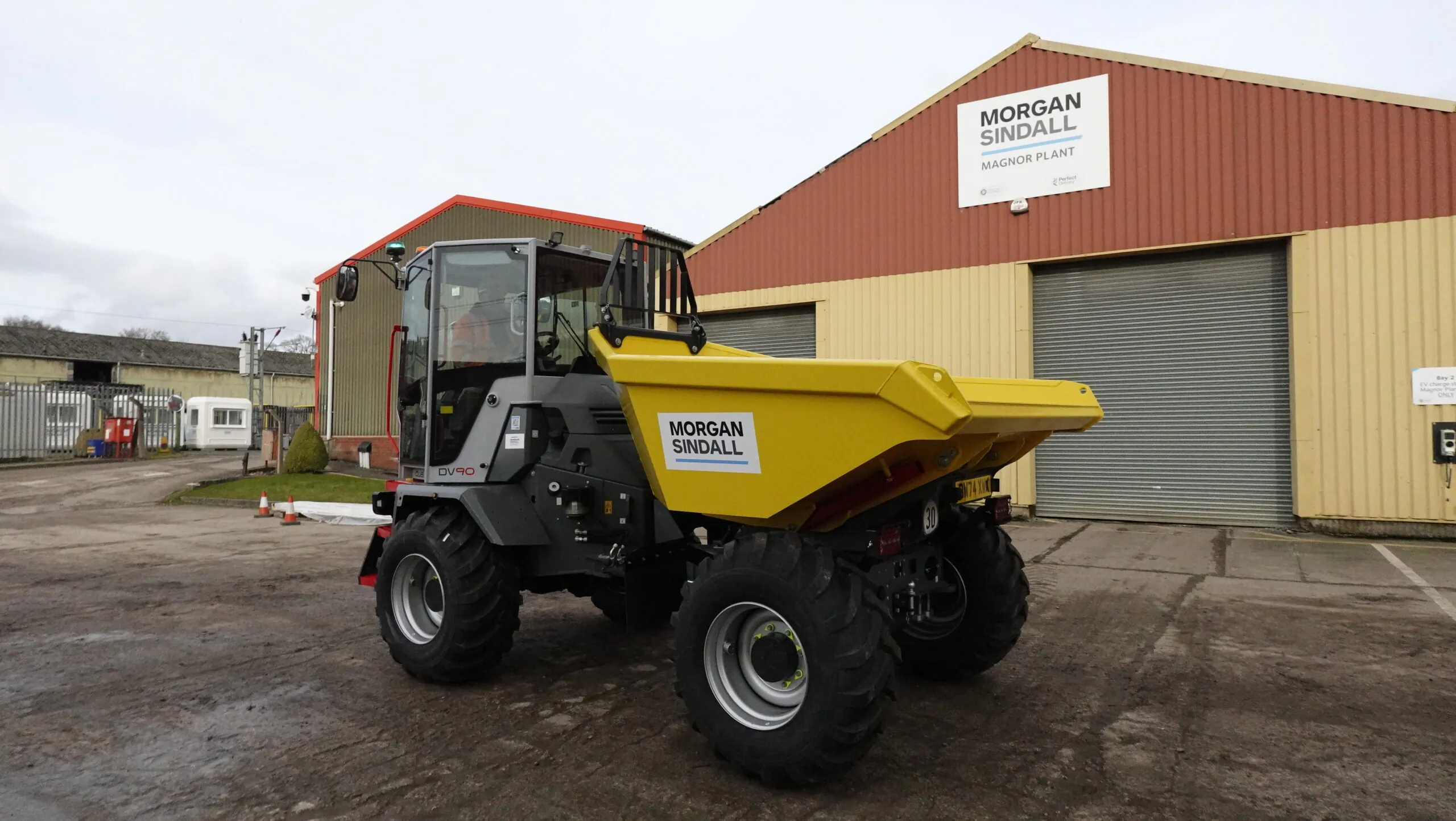 Large yellow dual-view dumper truck branded "Morgan Sindall" parked in front of the Morgan Sindall Magnor Plant building.